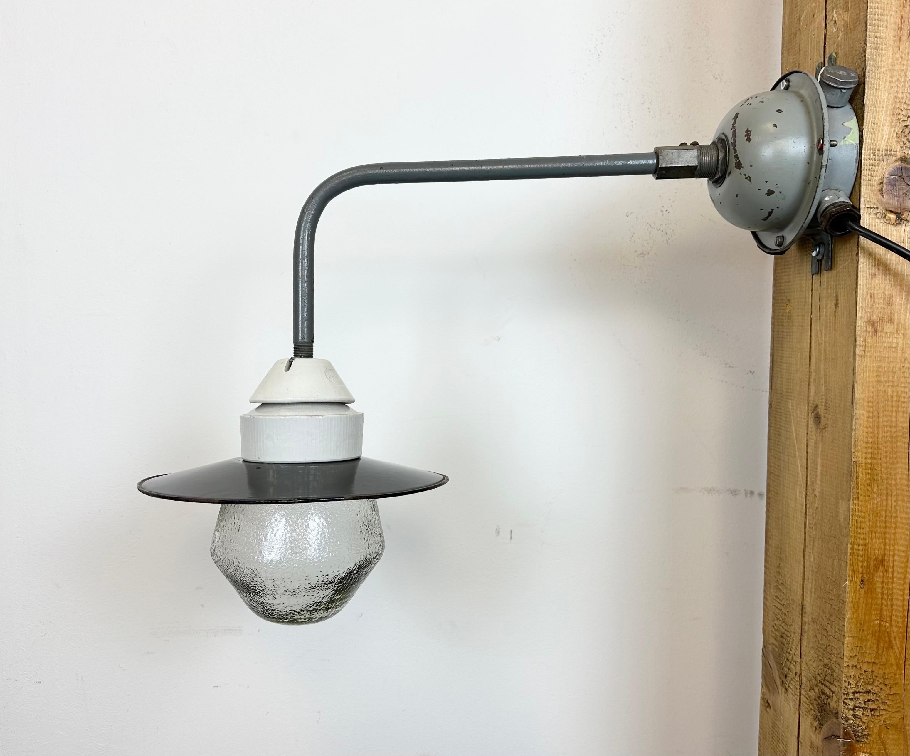 Industrial factory wall light made in Poland during the 1960s. It features a grey iron wall mounting and arm, a black enamel shade with white enamel interior, a porcelain top and a frosted glass cover.  The original socket requires standard E 27 / E