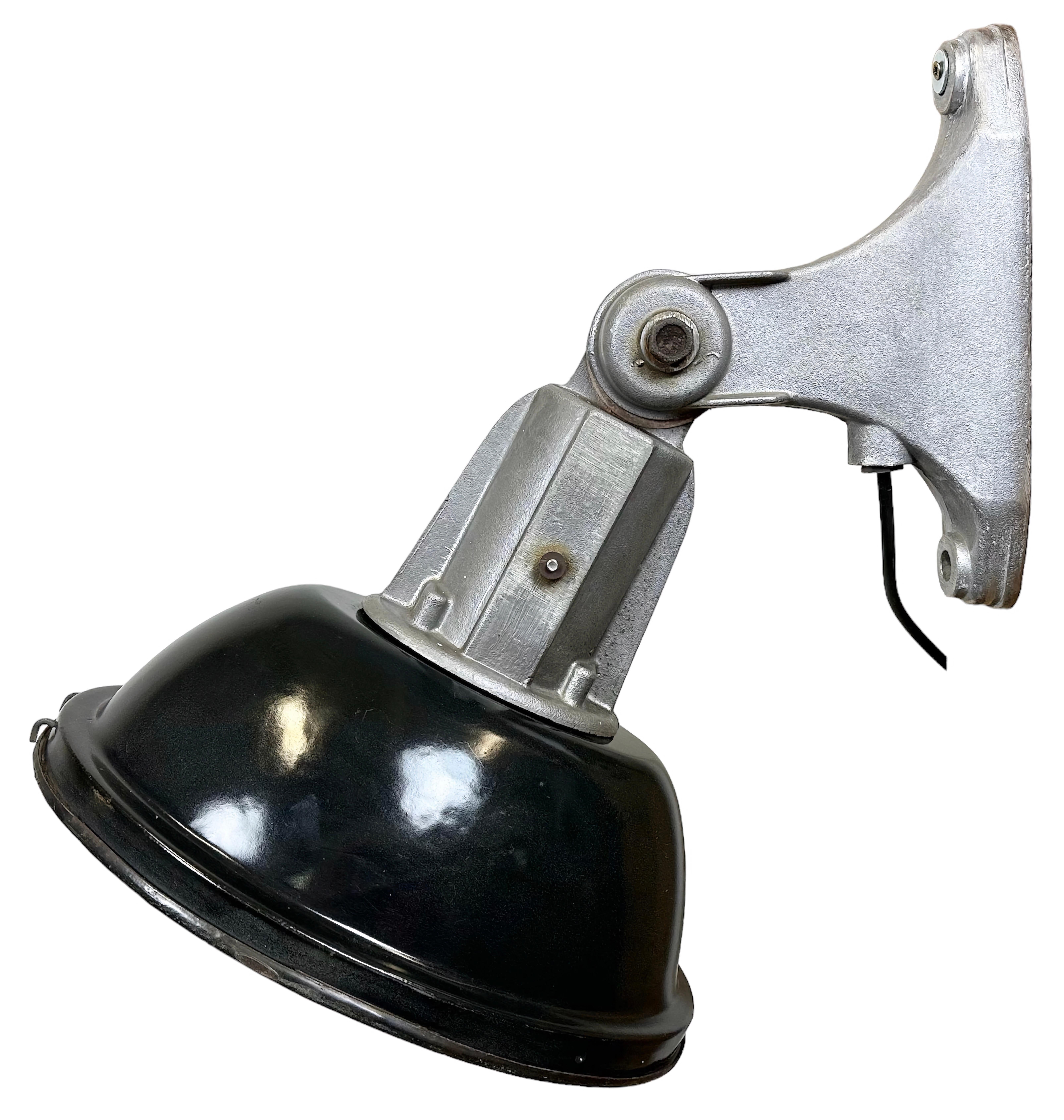Industrial wall light with adjustable angle made in France during the 1960s. It features a black enamel shade with white enamel interior, a cast aluminium wall mounting and an iron grid. The porcelain socket requires E27/E26 light bulbs. New