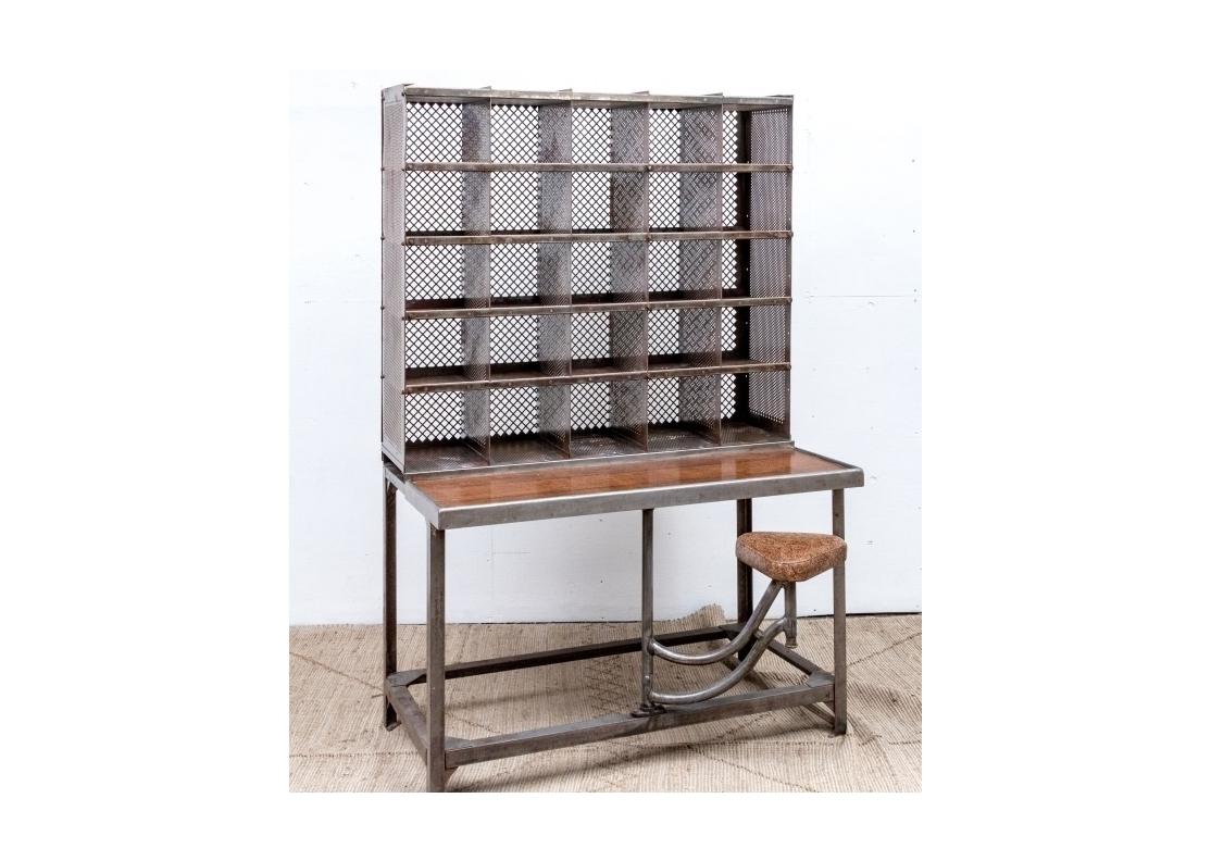 French steel postal sorting desk in two parts. The desk in two parts with upper having 25 open compartments with a grid back. The desk with an oak work surface and a swing away seat. The triangular seat covered in printed  vinyl.

Dimensions: 49