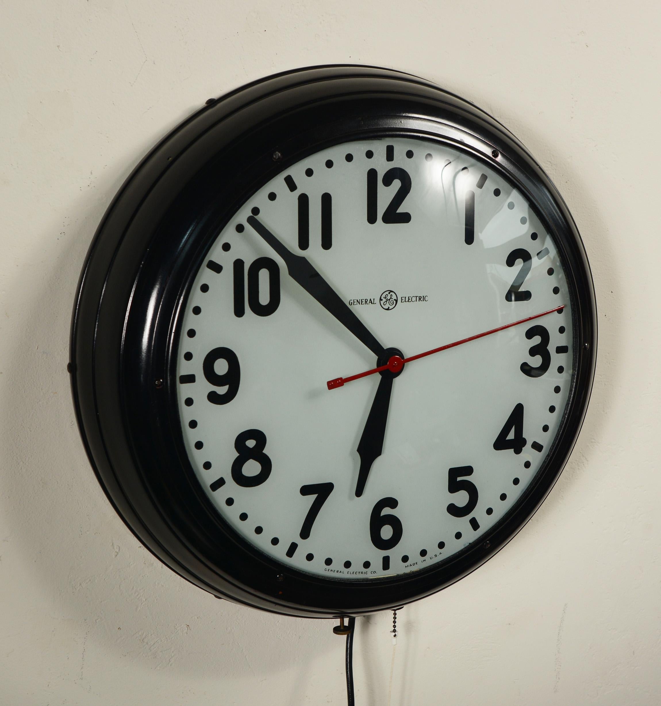 Large factory or school house style clock by General Electric. This clock has the harder to find lighted dial. The dial diameter is 14 inches. The clock has an older repaint and restoration. There are a couple of chips and scratches to the paint.