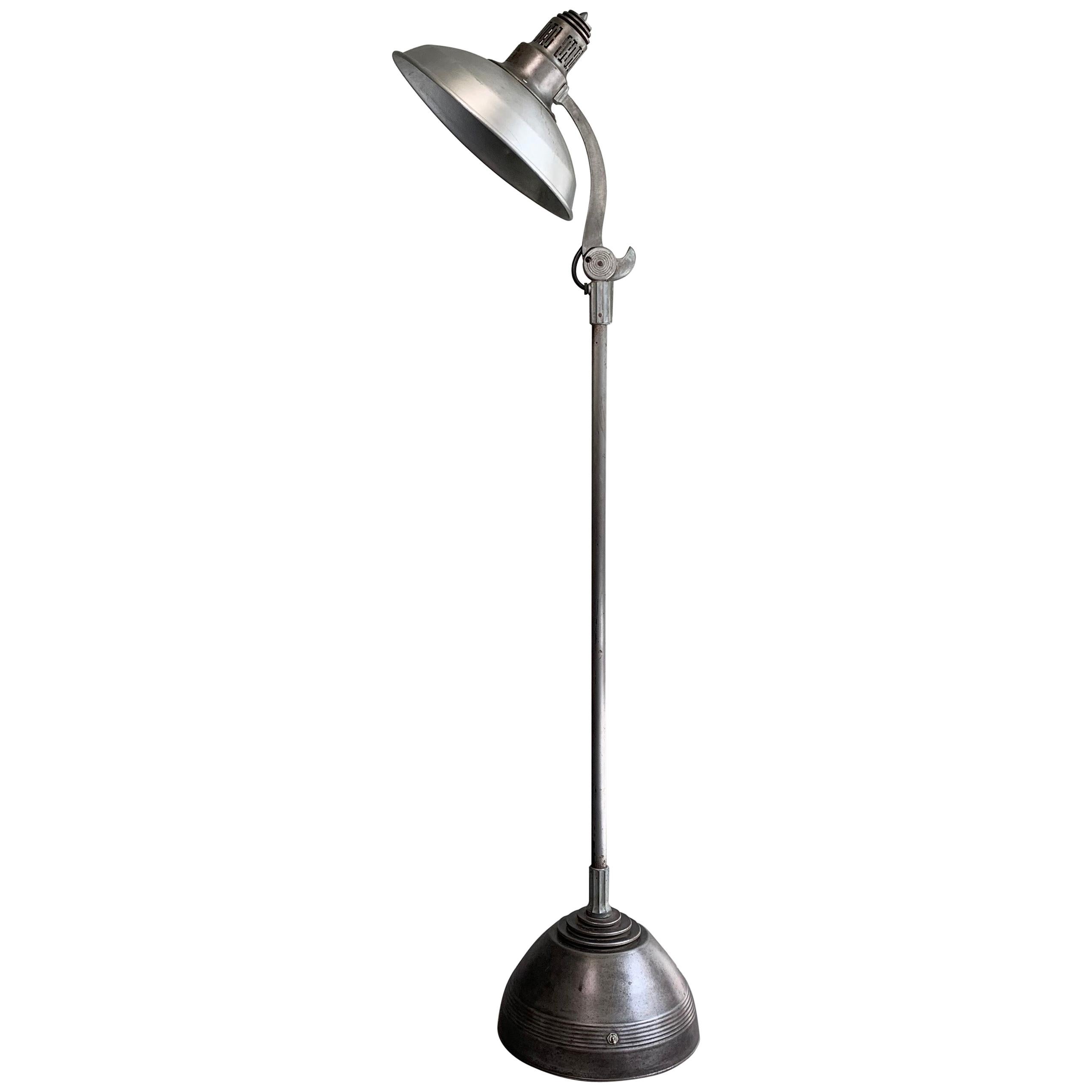 Industrial, Machine Age, brushed steel, General Electric sunlamp, medical floor lamp with wide 14.5 inch shade that adjusts up and down in 3 positions. The base is 12 inch diameter. The lamp is wired to accept a medium socket bulb up to 200 watts.