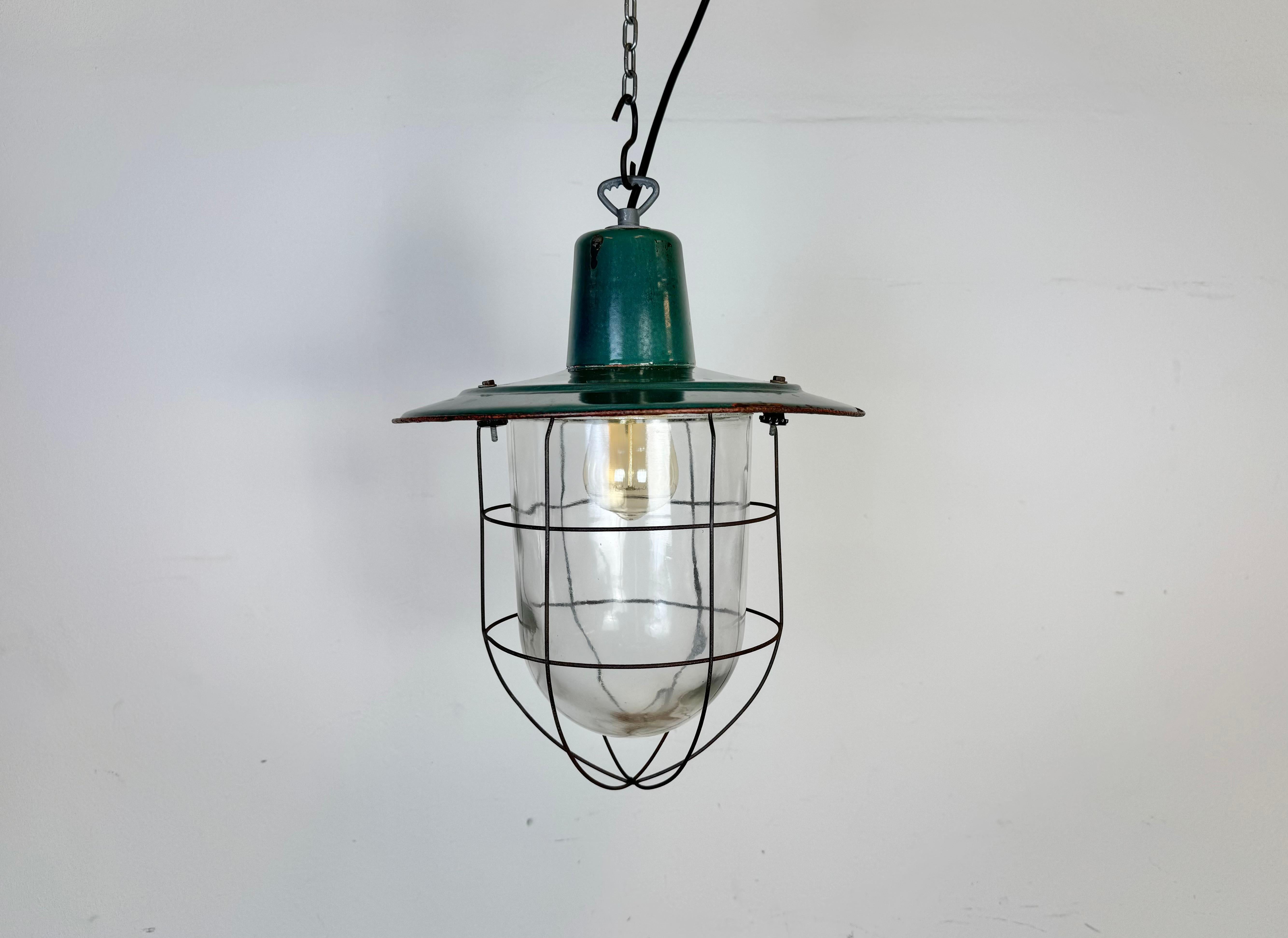 Industrial hanging lamp manufactured in Poland during the 1960s. It features a green enamel shade with white enamel interior, an iron top, a claer glass cover and iron grid. The porcelain socket requires standard  E 27/E 26 lightbulbs .New wire. The