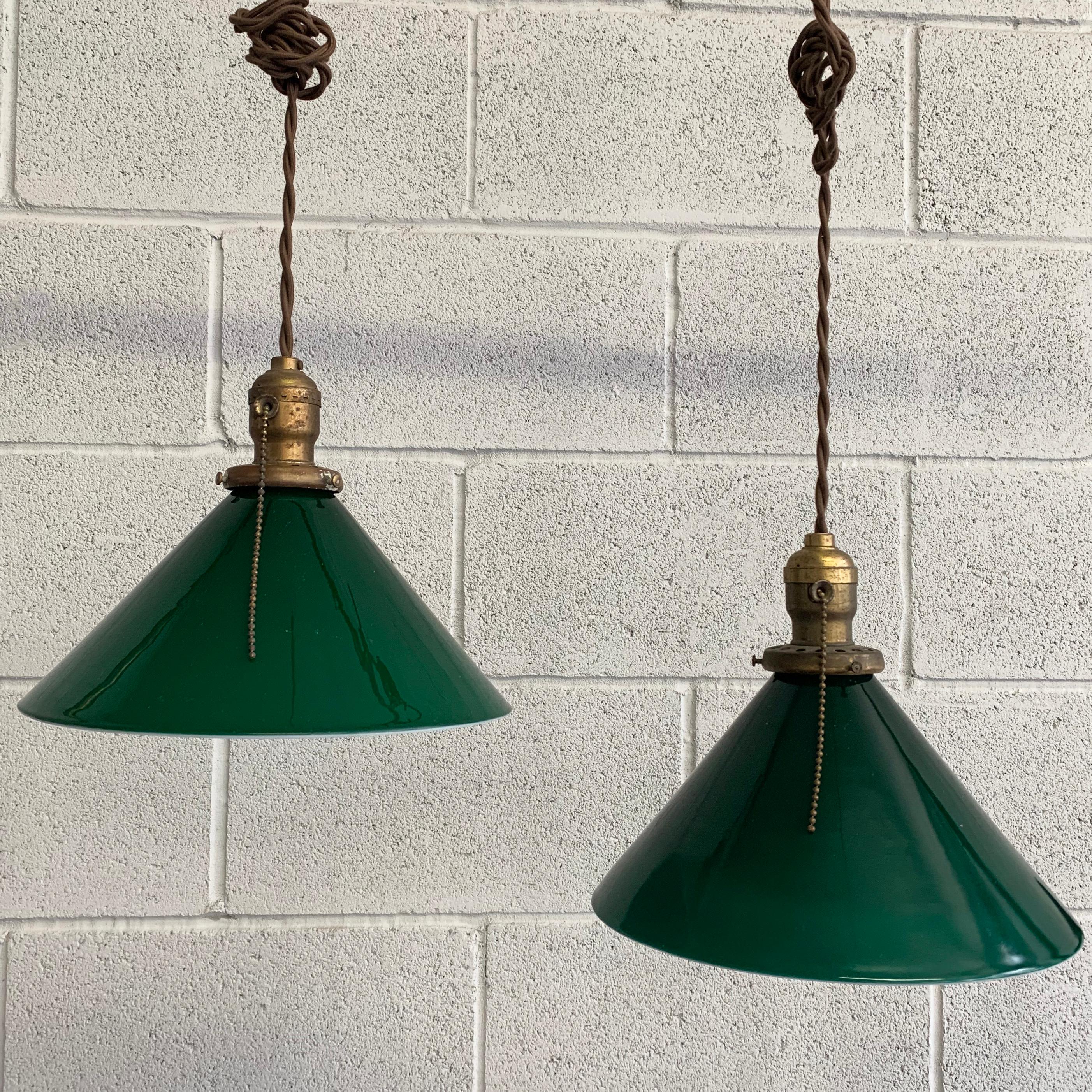 Industrial, early 20th century pendant lights feature green glass cone shades with brass pull chain fitters on 36 inches of braided cloth cord.