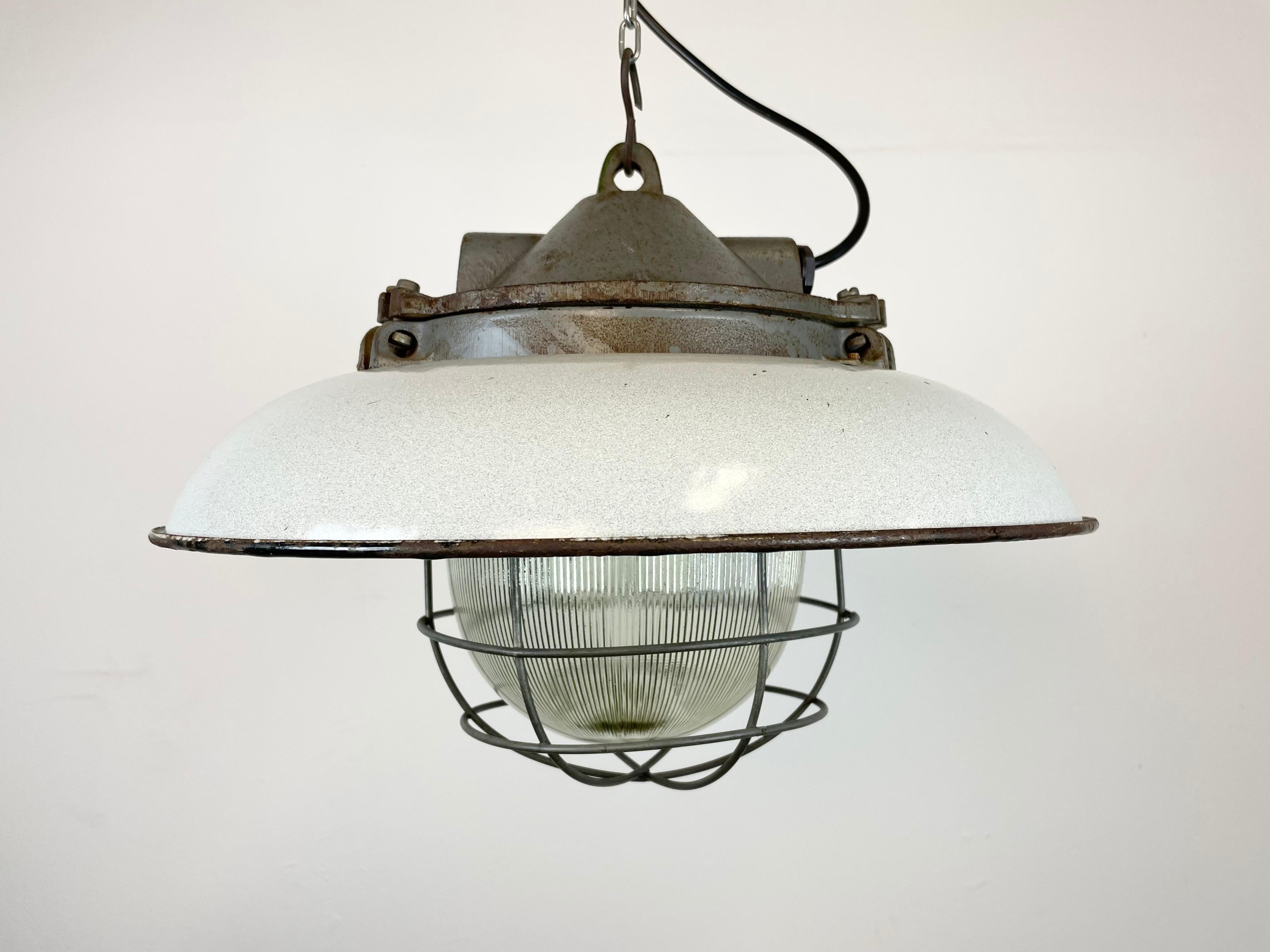 - Industrial factory pendant lamp in cast iron
- Manufactured by Zaos in Poland during the 1960s
- Light grey enamel shade with white enamel interior 
- Holophane glass cover and iron grid
- Weight: 7 kg.