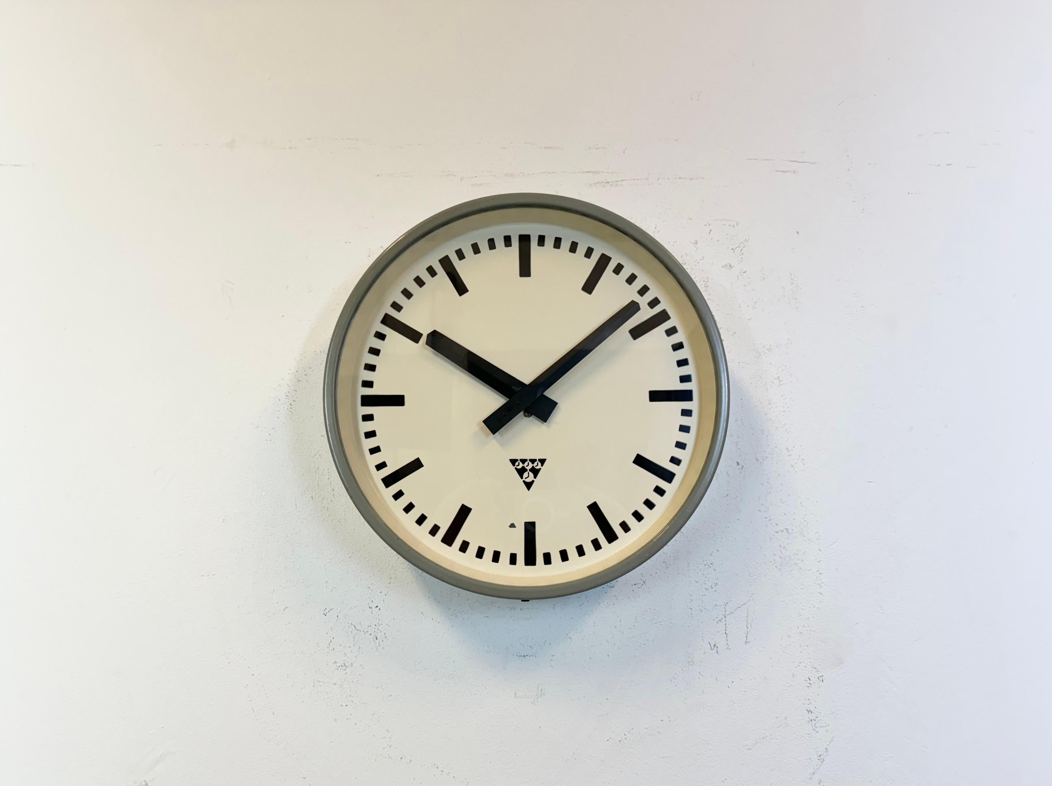 This wall clock was produced by Pragotron in former Czechoslovakia during the 1960s. It features a grey metal frame, an iron dial, an aluminium hands and a clear glass cover. Former factory electric slave clock has been converted into a