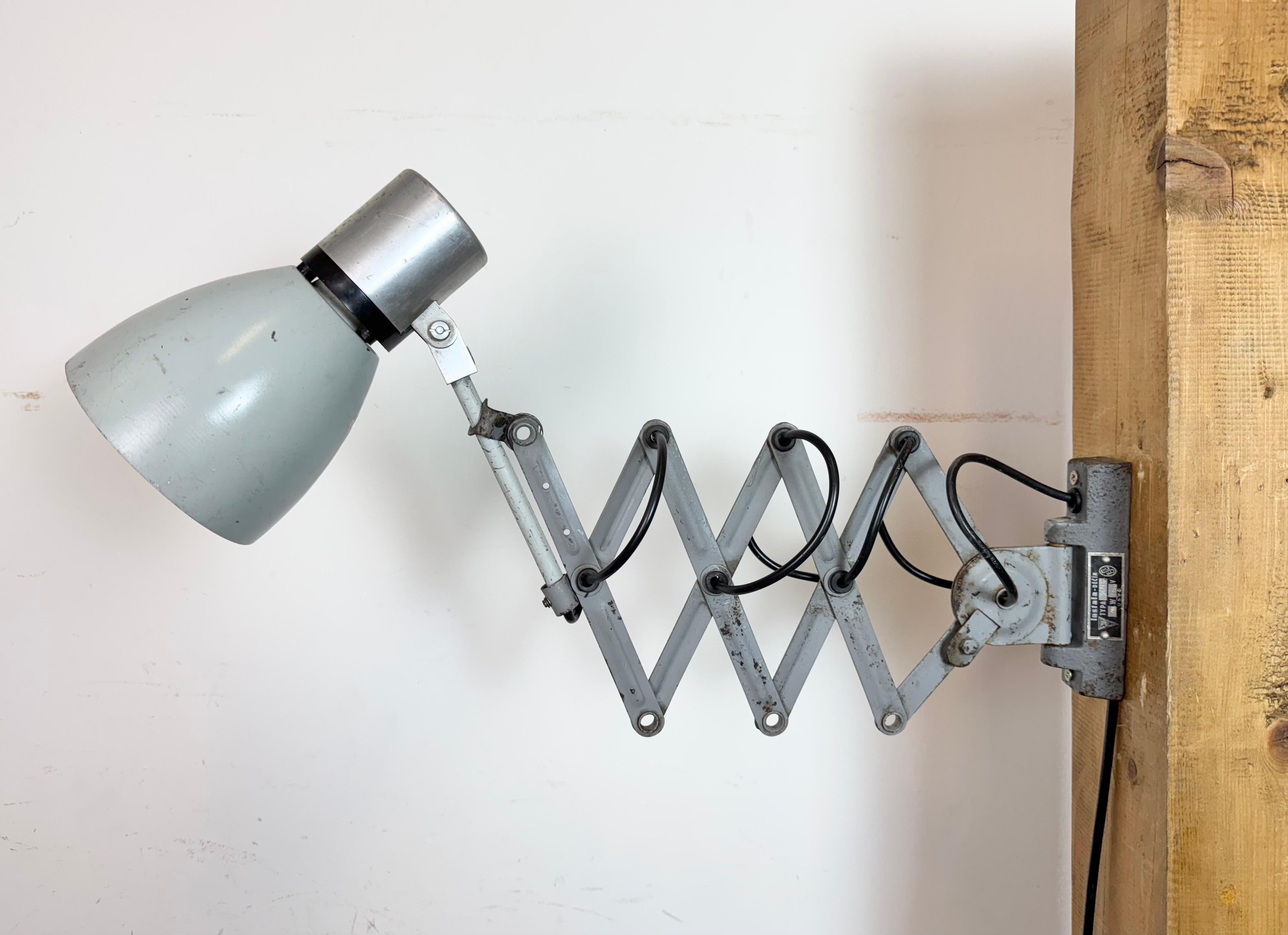 Diese verstellbare Industrie-Wandleuchte wurde in den 1960er Jahren in der ehemaligen Tschechoslowakei hergestellt. Die Leuchte hat einen Aluminiumschirm mit verchromter Spitze und einen grauen Scherenarm aus Eisen, der ausziehbar ist und zur Seite