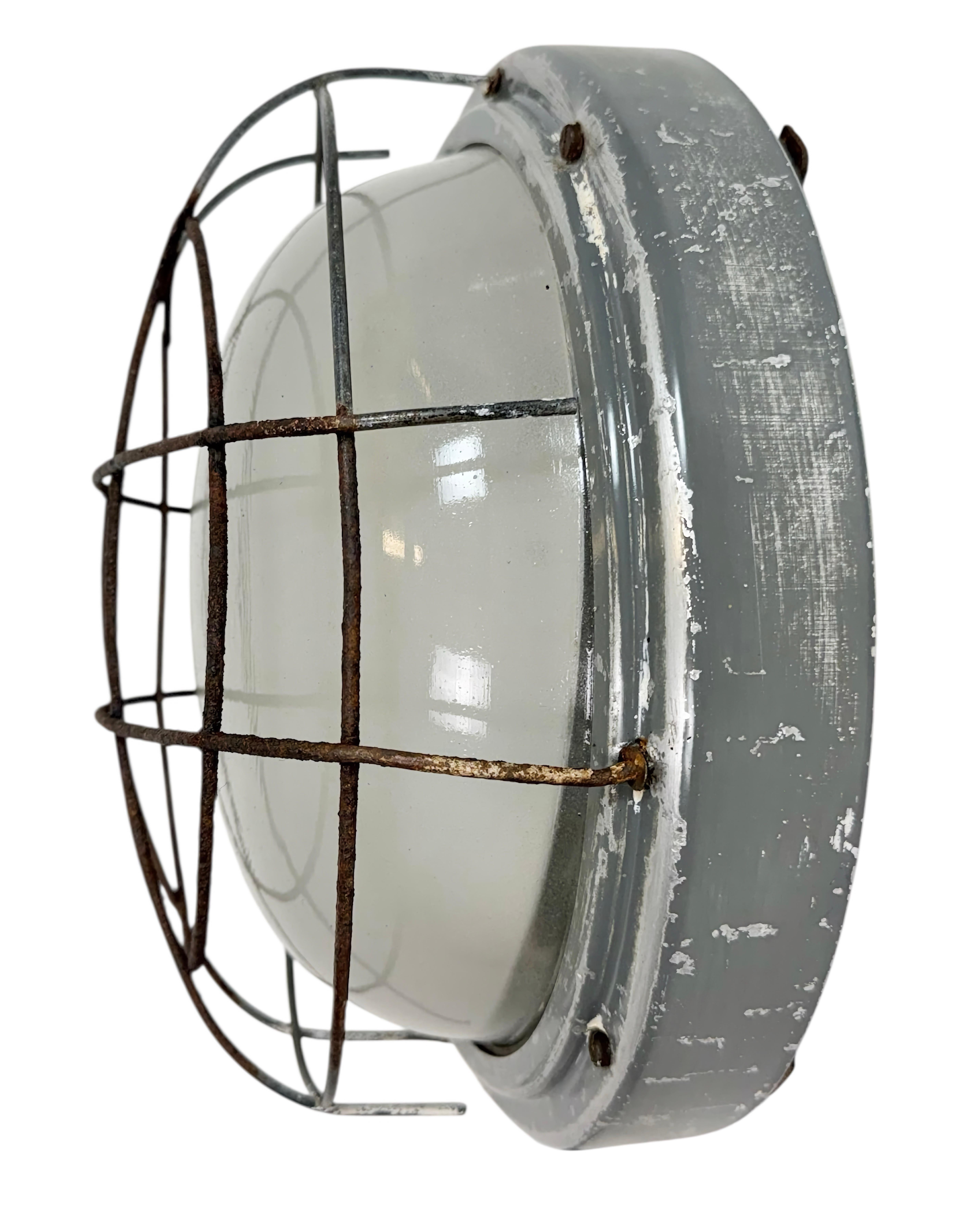 Este aplique industrial fue fabricado por Elektrosvit en la antigua Checoslovaquia durante la década de 1970. Presenta un cuerpo de metal gris, una tapa de cristal de leche y una rejilla de hierro oxidado. El casquillo requiere bombillas estándar