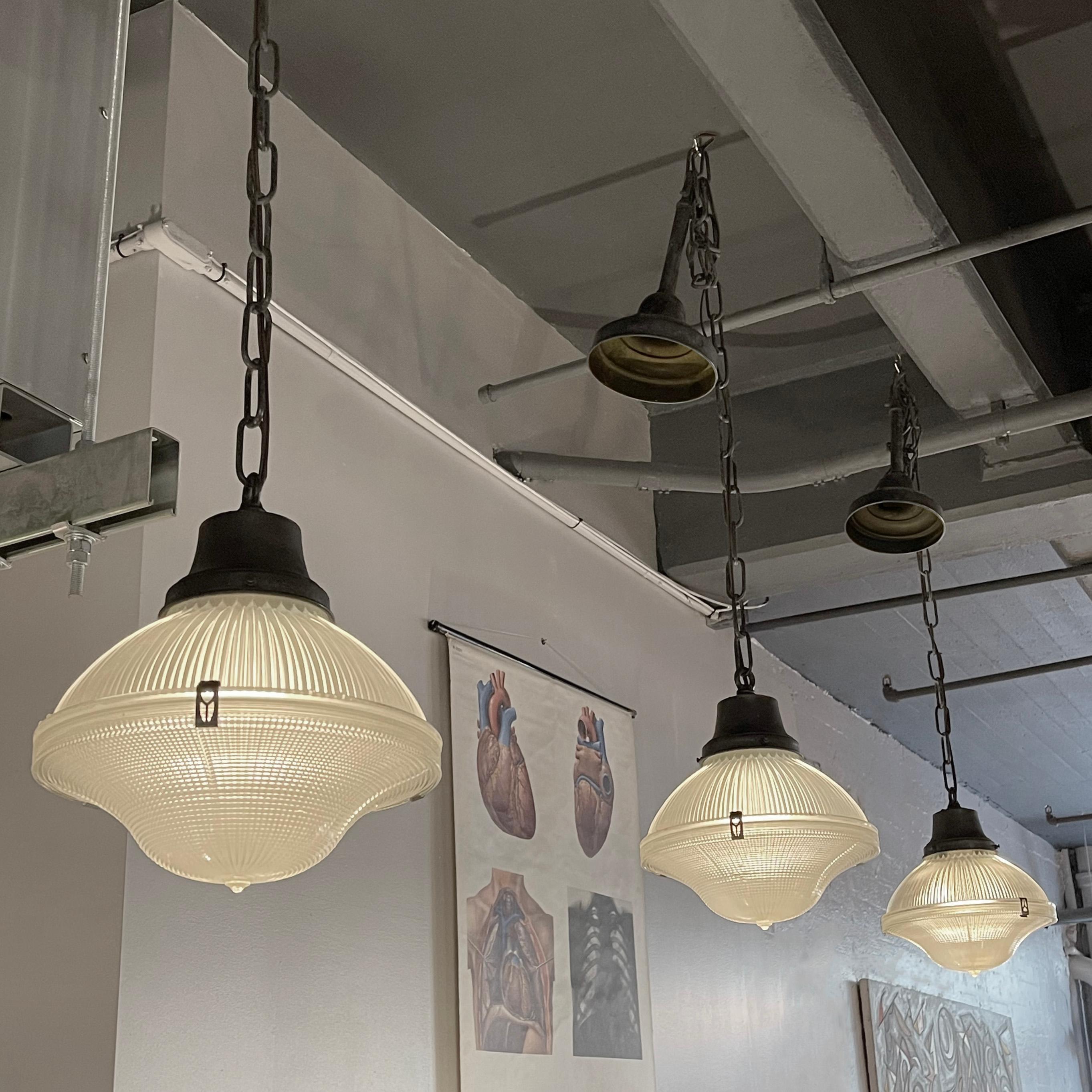 Trio of vintage, industrial, factory pendant lights feature 10 inches diameter, prismatic, double patterned, Holophane glass shades with steel clips and blackened steel fitters that hang on 36 inches of blackened steel chain and canopy. The lamps