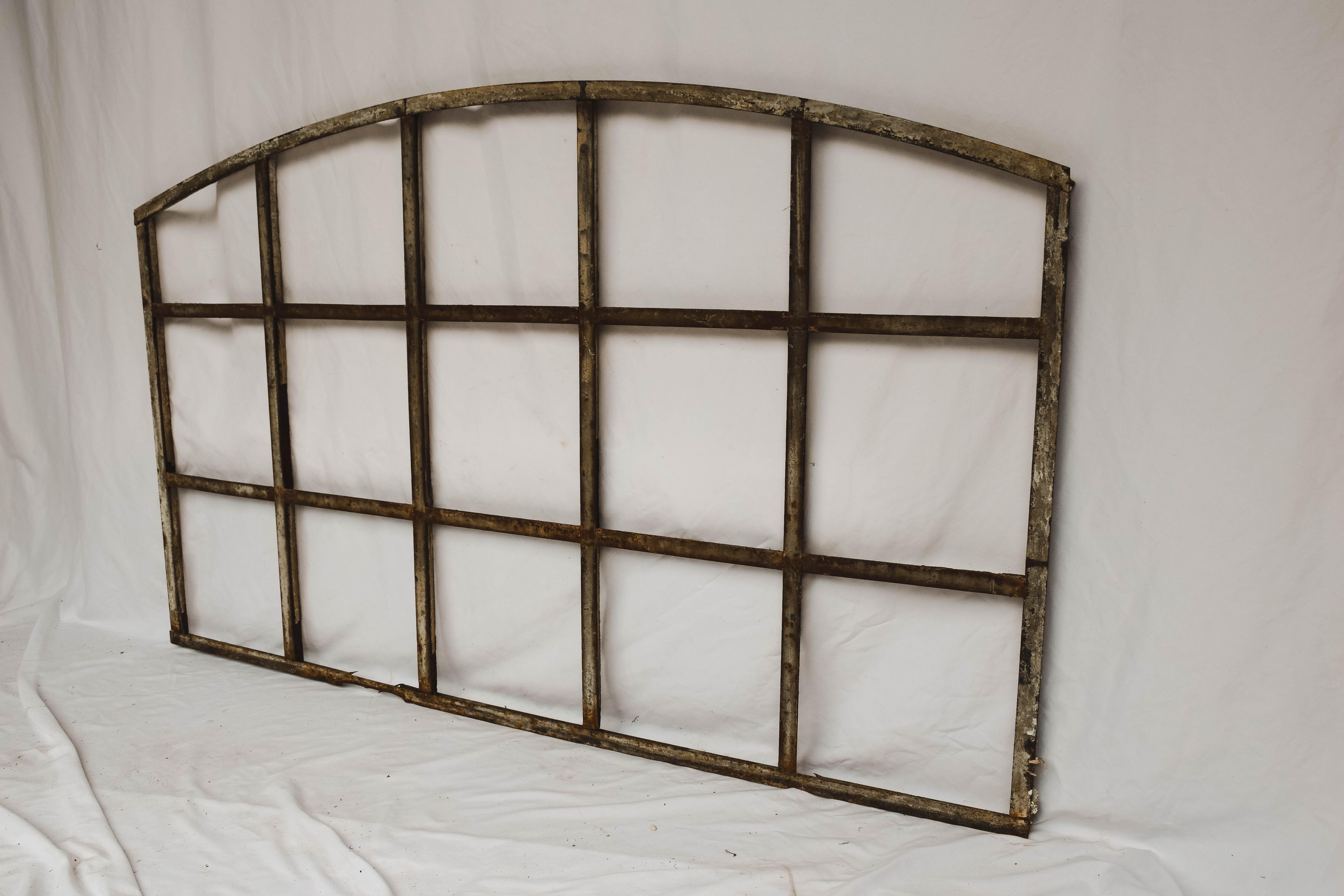 Imported from France, this industrial arched factory window frame (without the glass) has a lovely distressed and patinated metal finish with some old paint remnants. This handsome salvaged piece is constructed from iron with a thick frame for glass