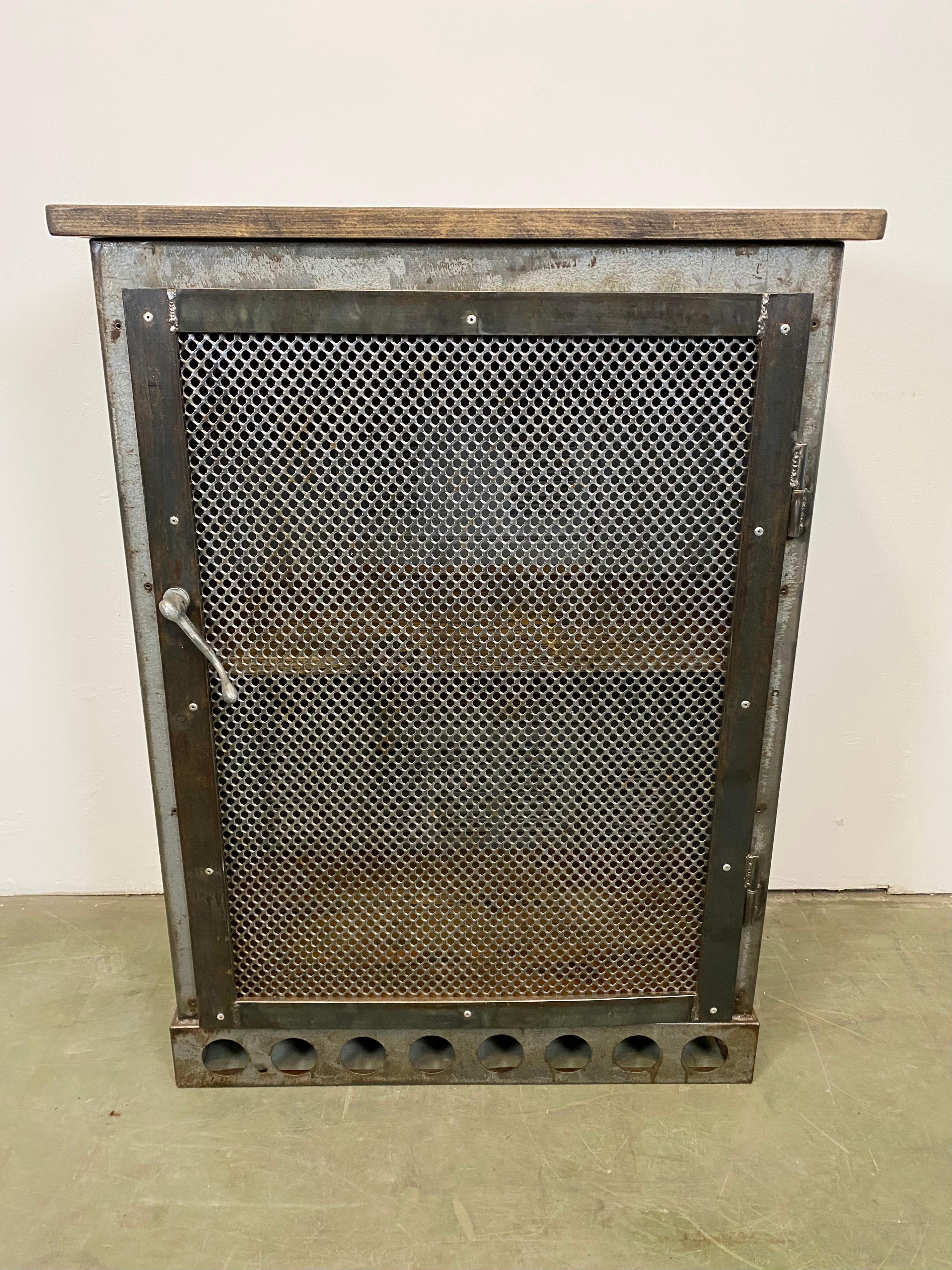 Iron cabinet from the 1960s it features an iron construction with mesh door, two wooden shelwes and wooden top. The weight of the cabinet is 55 kg.