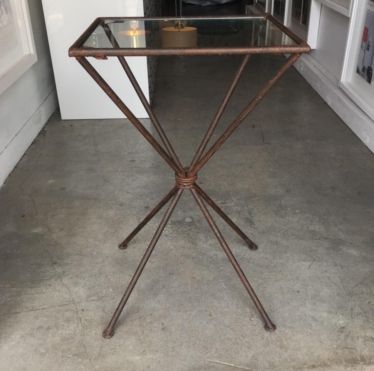 Great industrial side table hand welded of iron and has a glass top. The center has a roping cinched waist creating the flared legs. The table looks square however, it's a rectangle by 2 inches. The hand welding is visible in areas adding to its