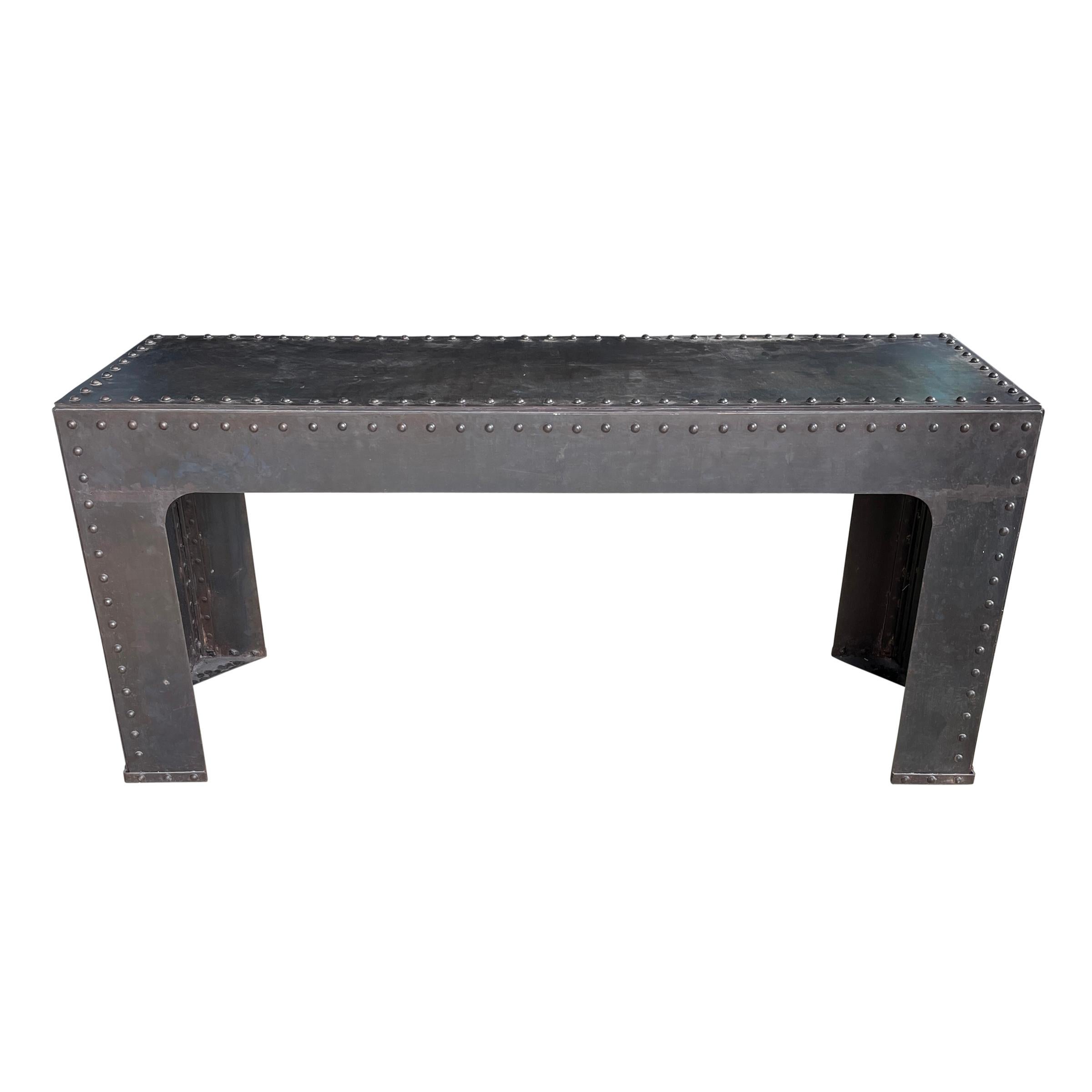 An extraordinary and memorable American Industrial steel console table with rivets covering the top and sides, and sides with arched cutouts. Perfect behind your sofa, in your entry, or under a TV in your living room.