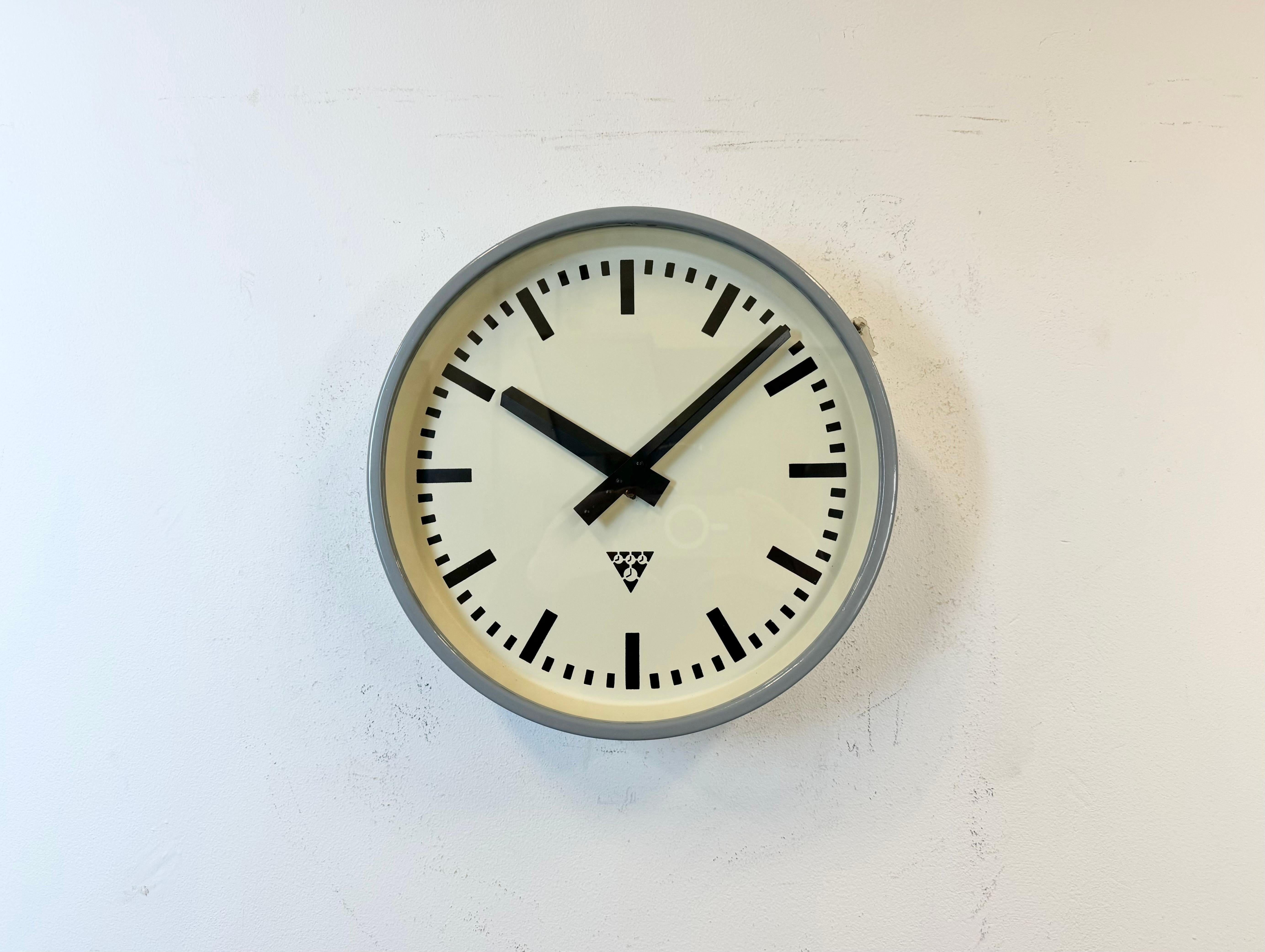 This wall clock was produced by Pragotron in former Czechoslovakia during the 1960s. It features a light grey metal frame, an iron dial, an aluminium hands and a clear glass cover. Former factory electric slave clock has been converted into a