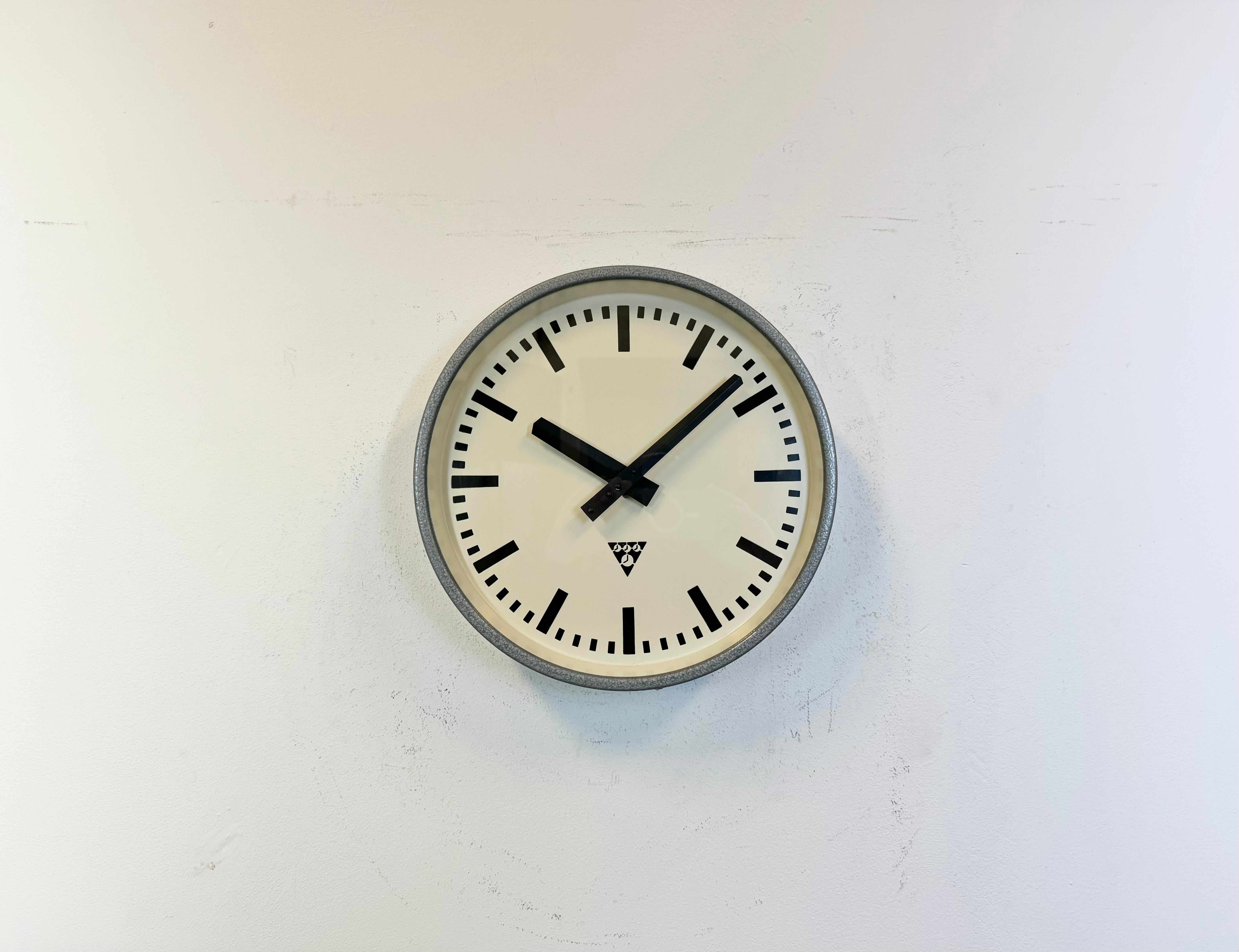 This wall clock was produced by Pragotron in former Czechoslovakia during the 1960s. It features a grey hammer paint metal frame, an iron dial, an aluminium hands and a clear glass cover. Former factory electric slave clock has been converted into a