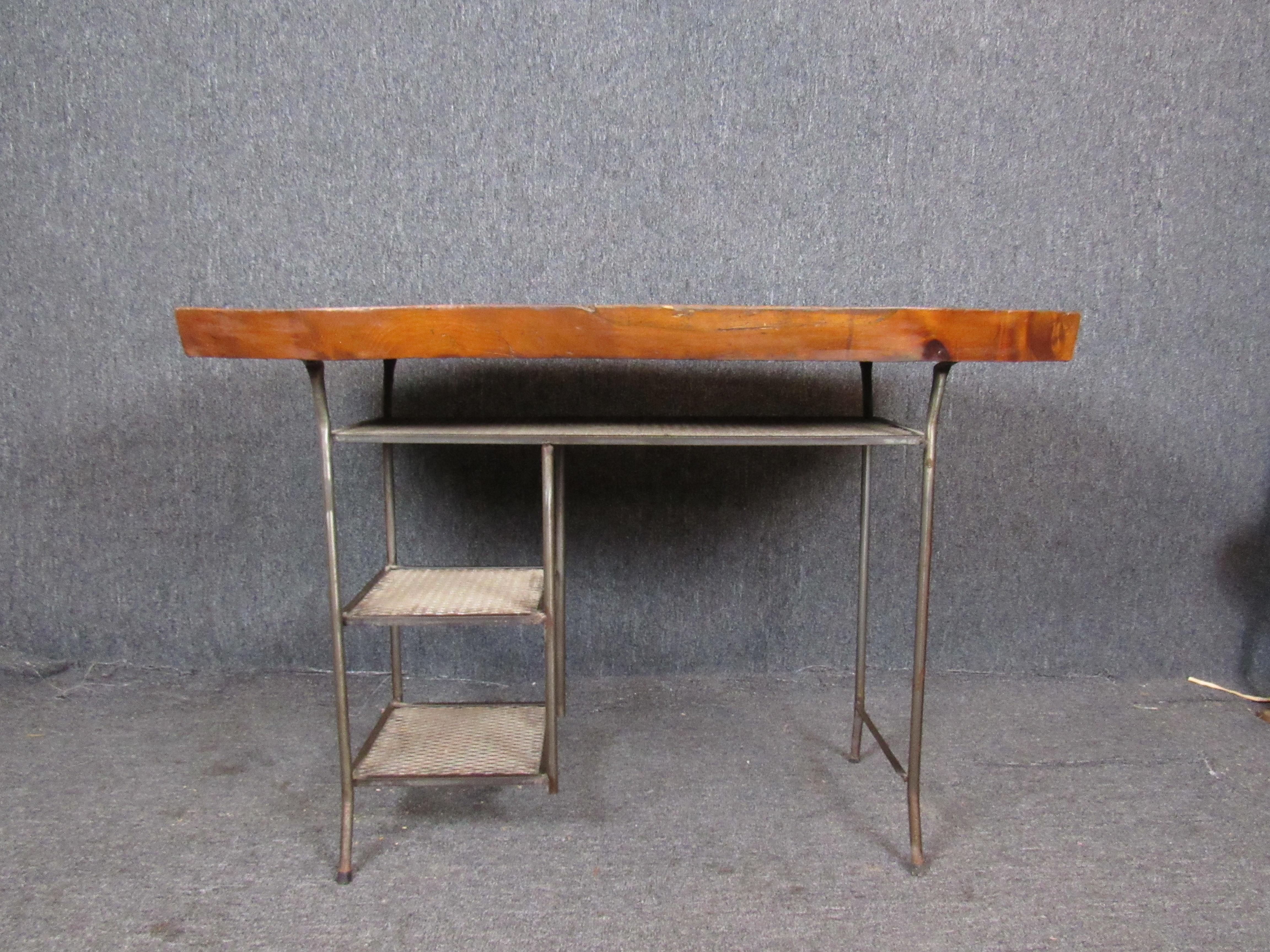 Absolutely fantastic writing desk, seamlessly blending nature and machine. A sturdy live edge slab desktop offers ample workspace for any project on hand. An industrial iron base features three shelves, lending functionality and style. Please