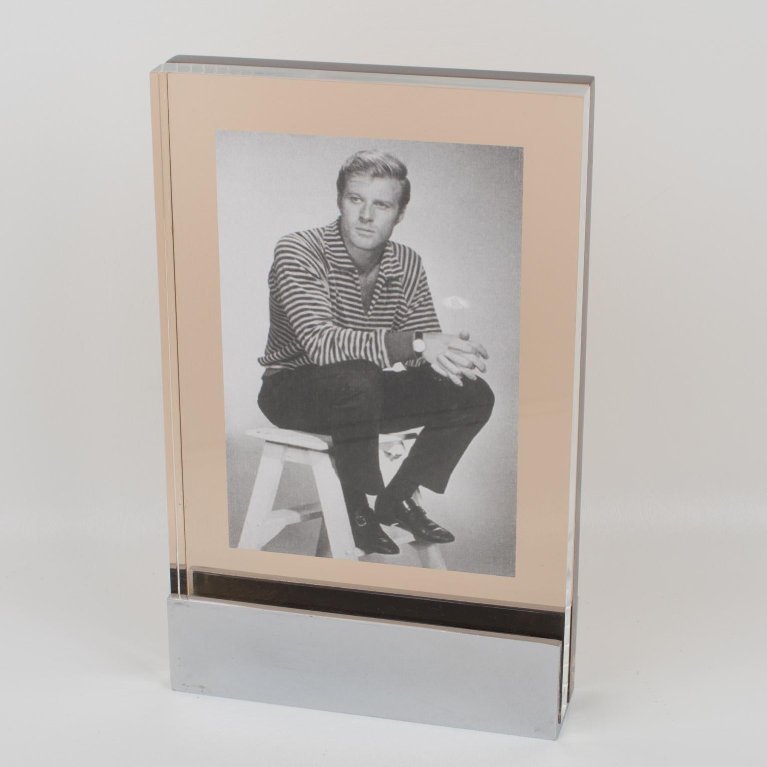 This is a beautiful French Machine Age metal and Lucite photo frame with a modernist industrial design from the 1960s. The chromed metal base holder has visible screws and holds the photography between two extra-thick Lucite slabs, one transparent