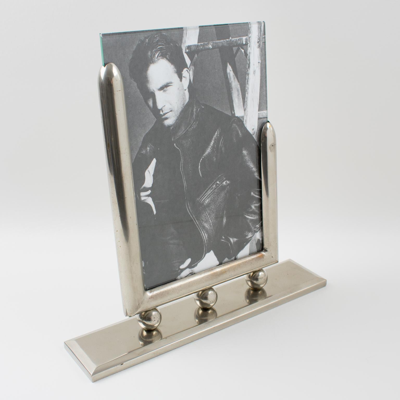 This impressive Machine Age metal picture photo frame boasts a modernist industrial design with geometric holders on a large metal plinth. Two glass sheets complete the frame to enclose the photograph. There is no visible maker's mark.
The photo