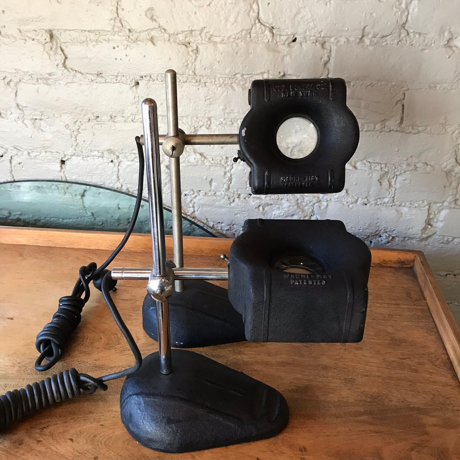 Magni-ray, midcentury, industrial, magnifying, jeweler's table lamps feature cast metal bases and shades with chrome poles and stems. The lamps are height adjustable and can turn 360 degrees with room for 2 bulbs.