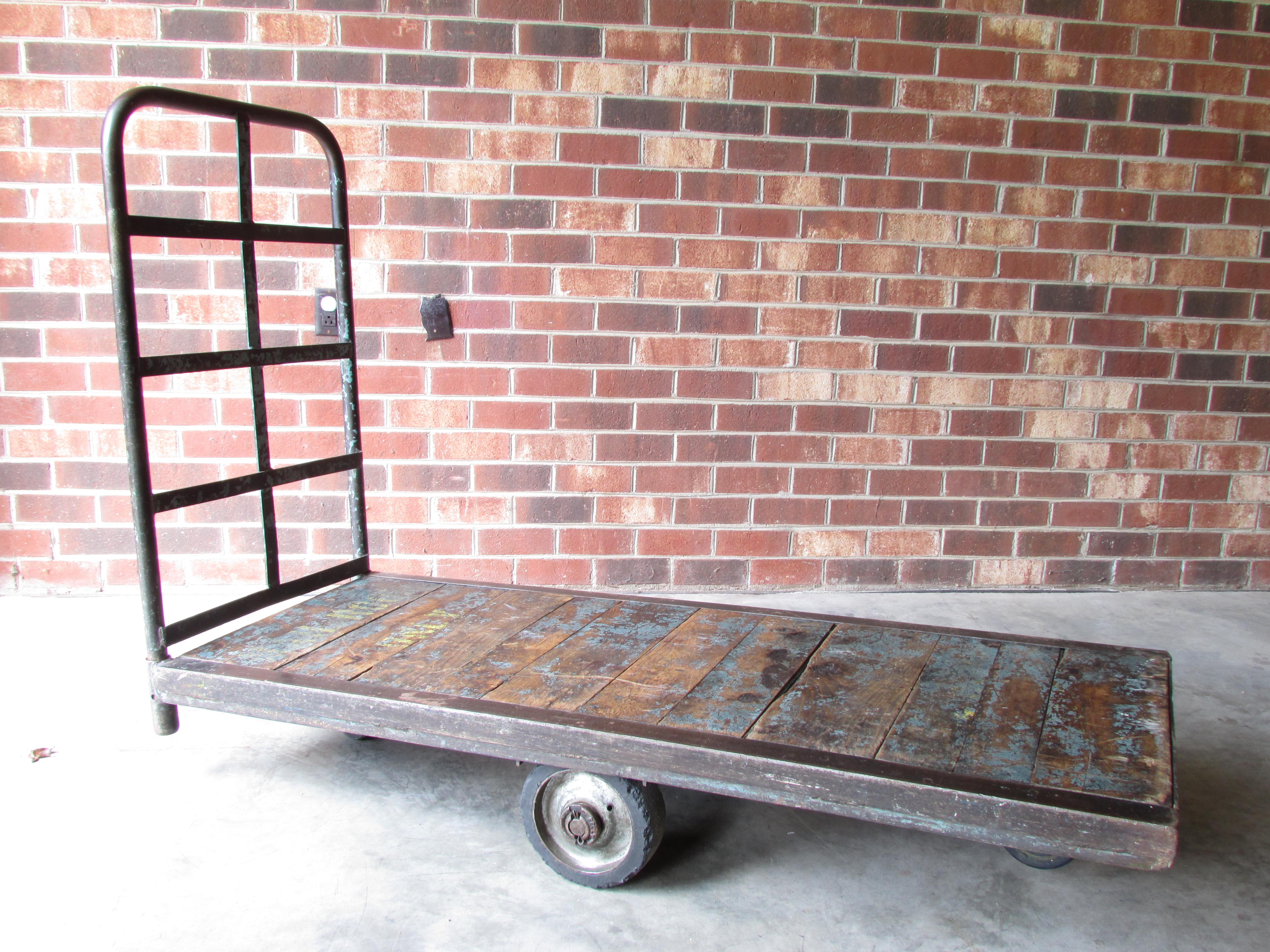 Worn and weathered antique rolling Industrial cart with metal frame and wooden slat deck has removable metal handle and brace and 