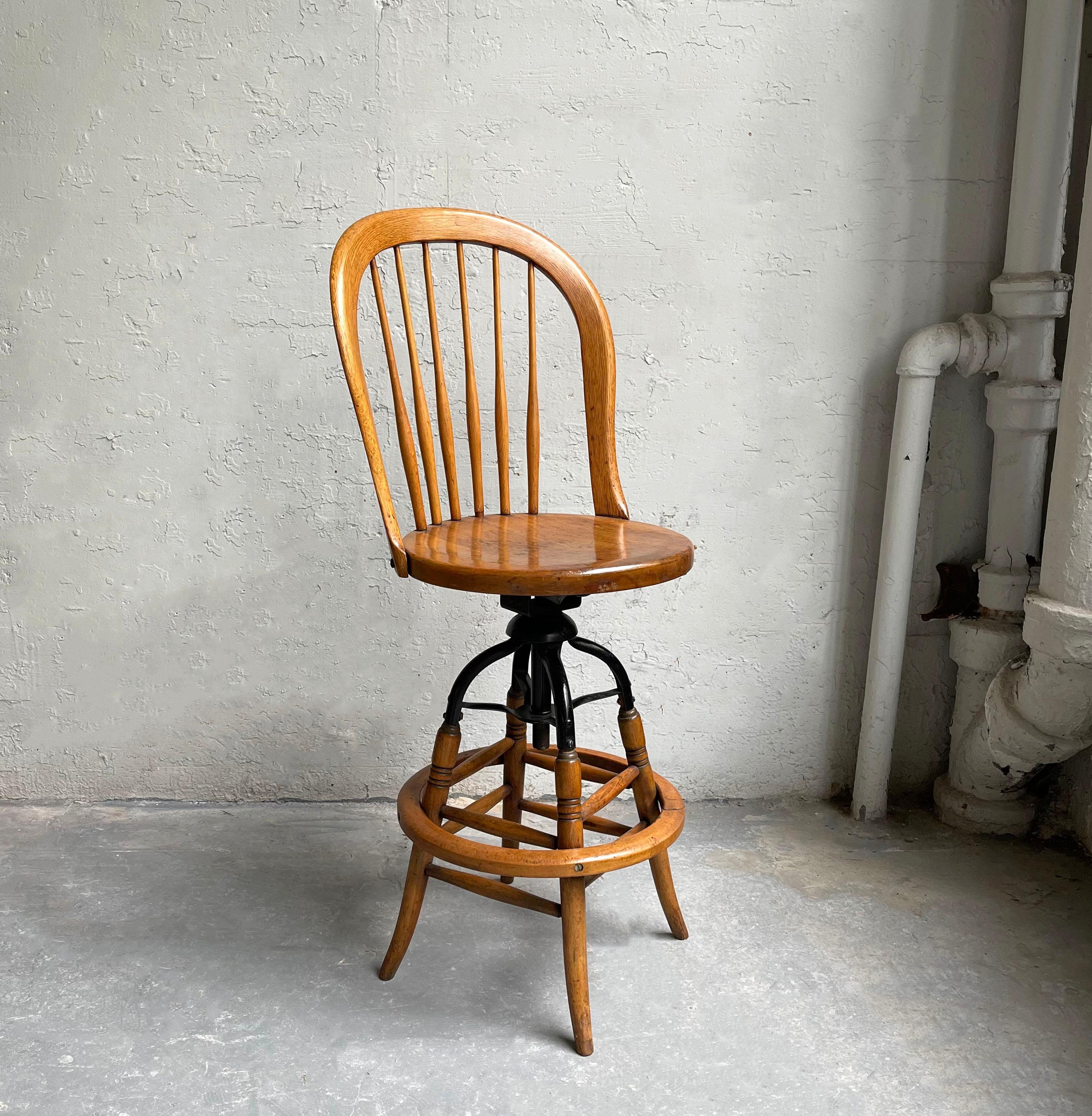 Antique, late 19th century, industrial, maple and steel, drafting stool features a sculpted spindle back with turned details on the legs. The stool is height adjustable to approx 30 inches.