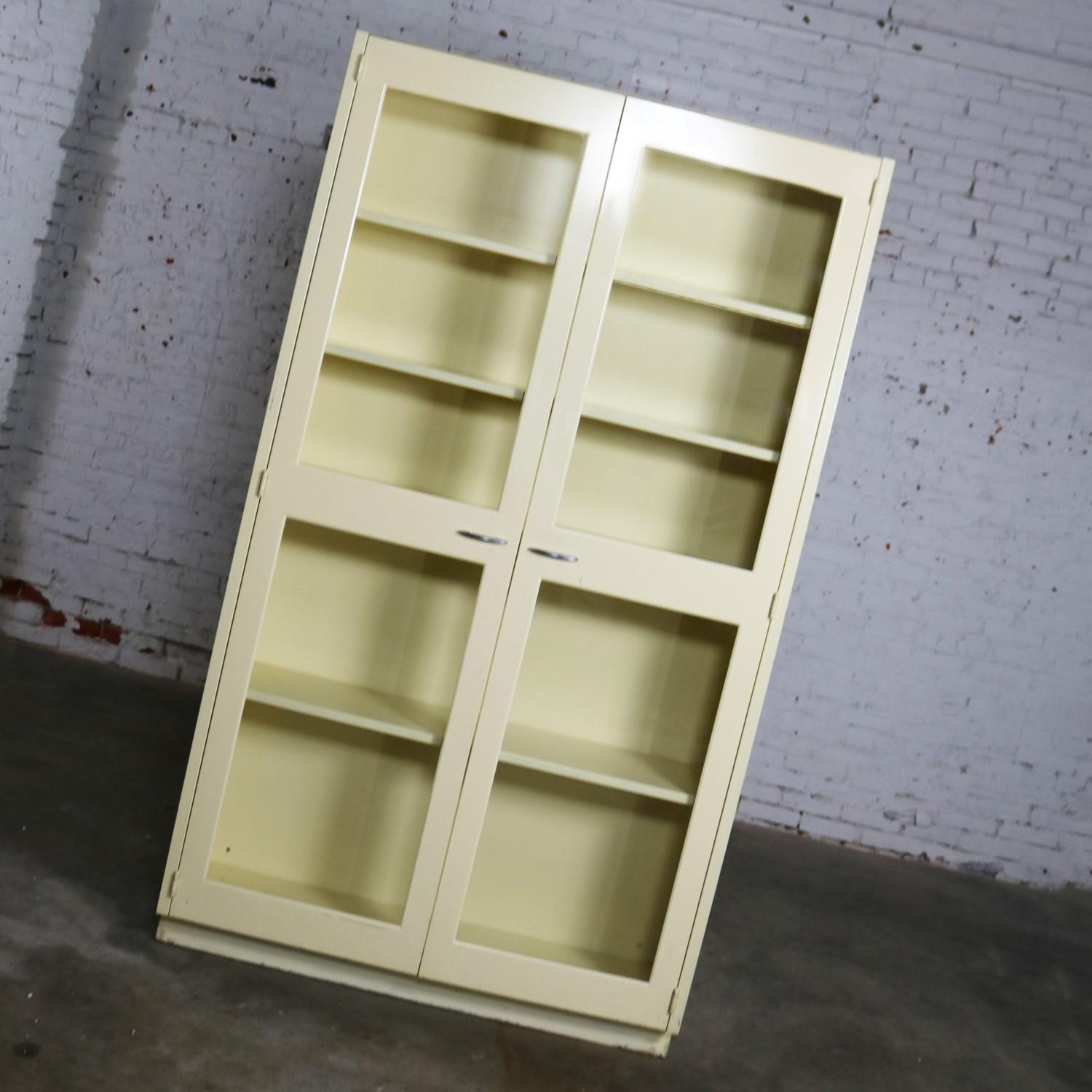 Awesome industrial metal storage cabinets with glass double opening doors. Fabulous for display or as a bookcase. They are both in wonderful vintage condition, and the ivory painted finish has a nice age patina including scratches and nicks. Please
