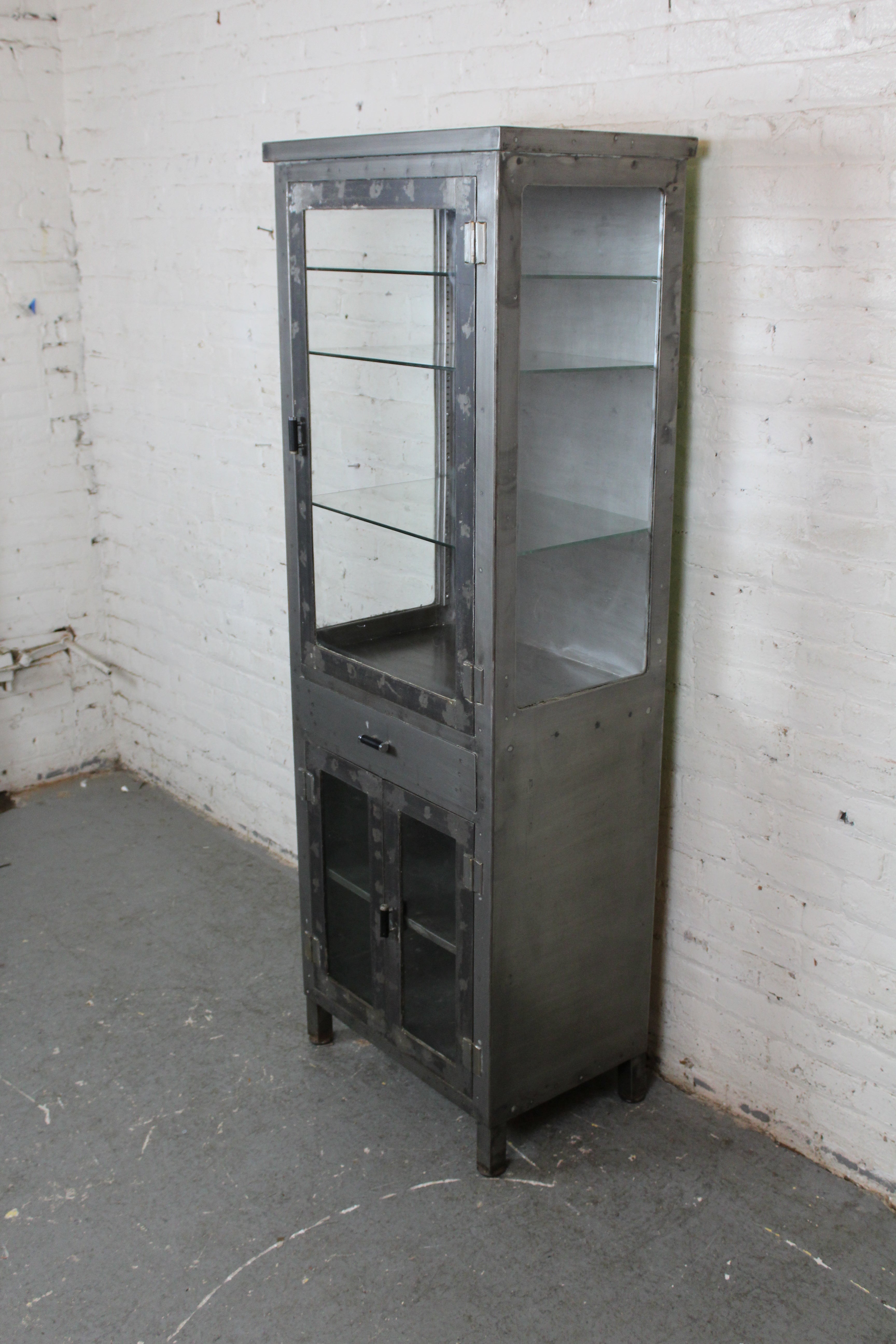 Cette armoire métallique industrielle robuste, tout droit sortie de l'ère des machines, apporte une touche de présence grinçante à n'importe quel espace ! D'une hauteur de près de 2 mètres, cette structure en acier comprend une grande vitrine avec