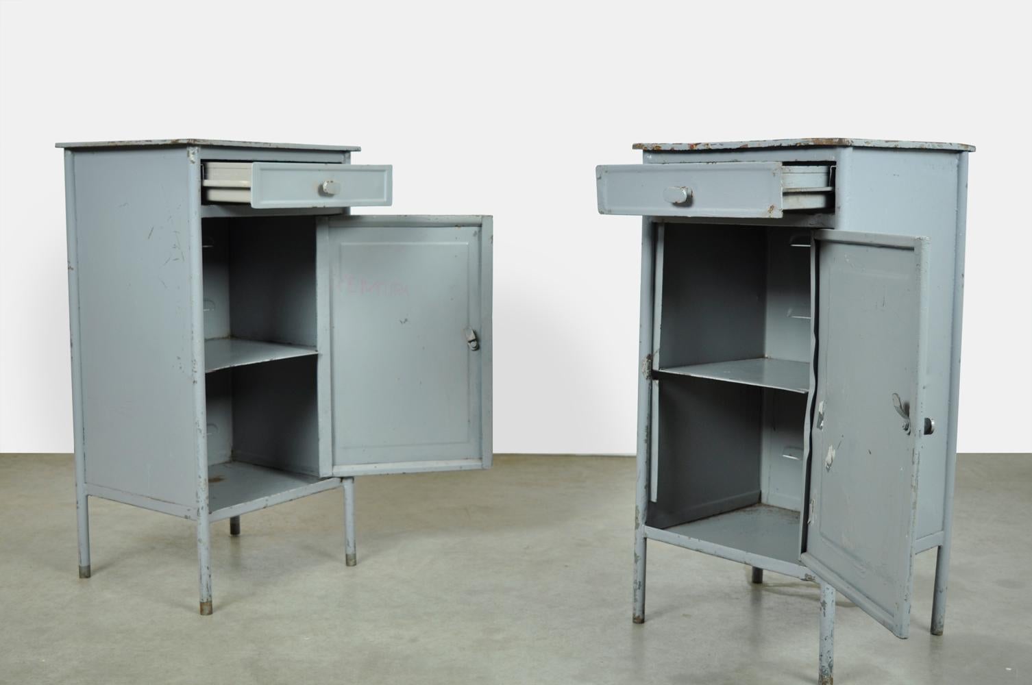 industrial metal hospital cabinets with an origin in Eastern Europe, 1960s. The metal lockers have four slender legs, a cabinet with a door and a drawer that can be closed with a steel rotary knob. Nice to use as a bedside table, side table or as a