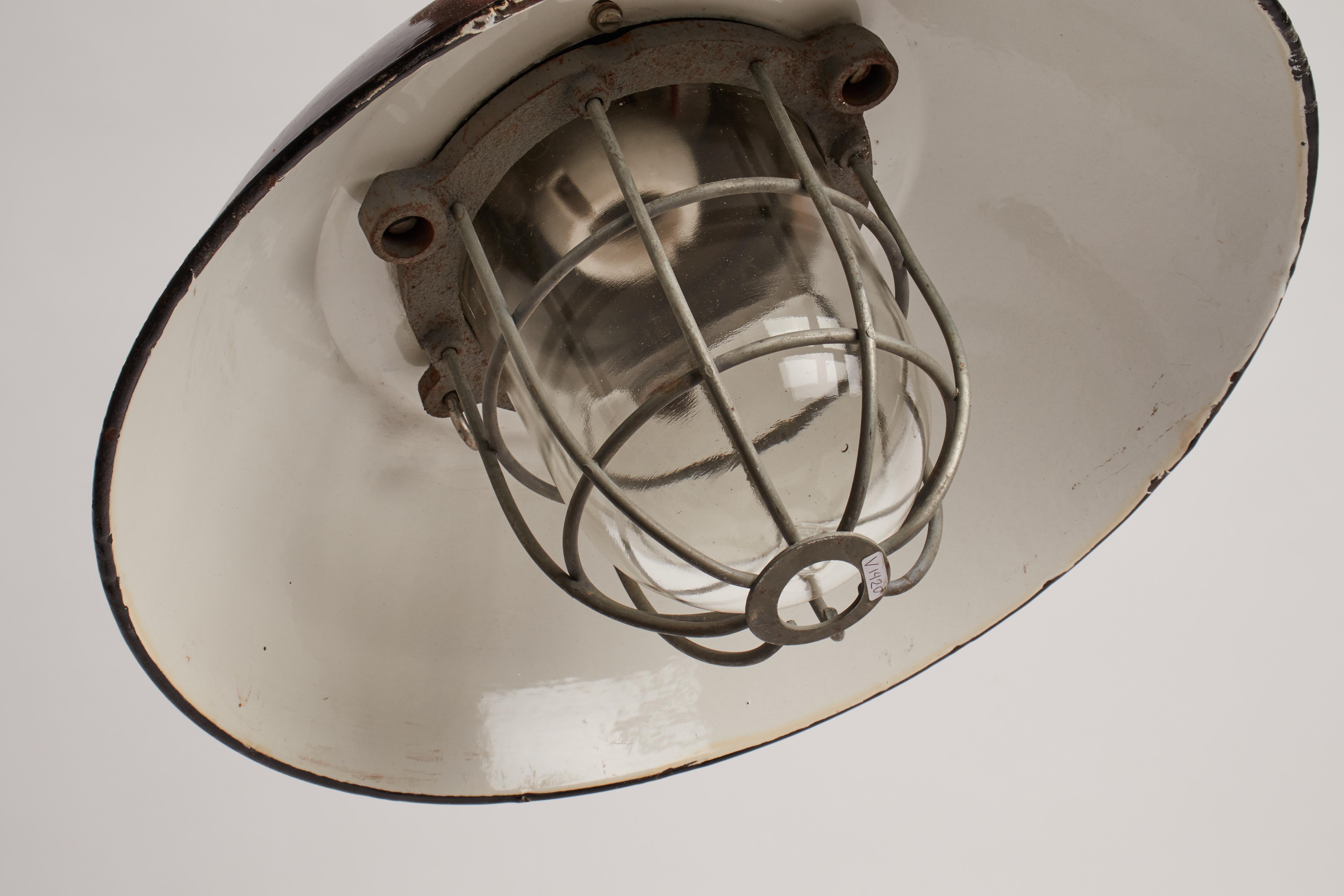 Industrial ceiling lamps with cast iron top, enameled dome shaped shade and cast iron caged, thick glass. Original patina. Six pieces available, priced per light. Prague, 1900 ca.