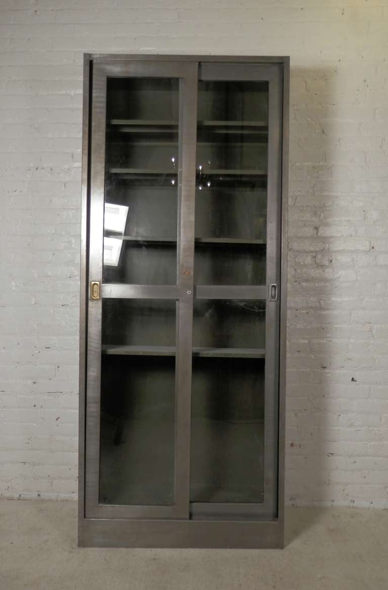 Large metal cabinet with two sliding doors, newly re-finished in a bare metal machine age look. Four adjustable metal shelves included. Unique brass detailing. Perfect as a pantry or display cabinet.

(Please confirm item location - NY or NJ -