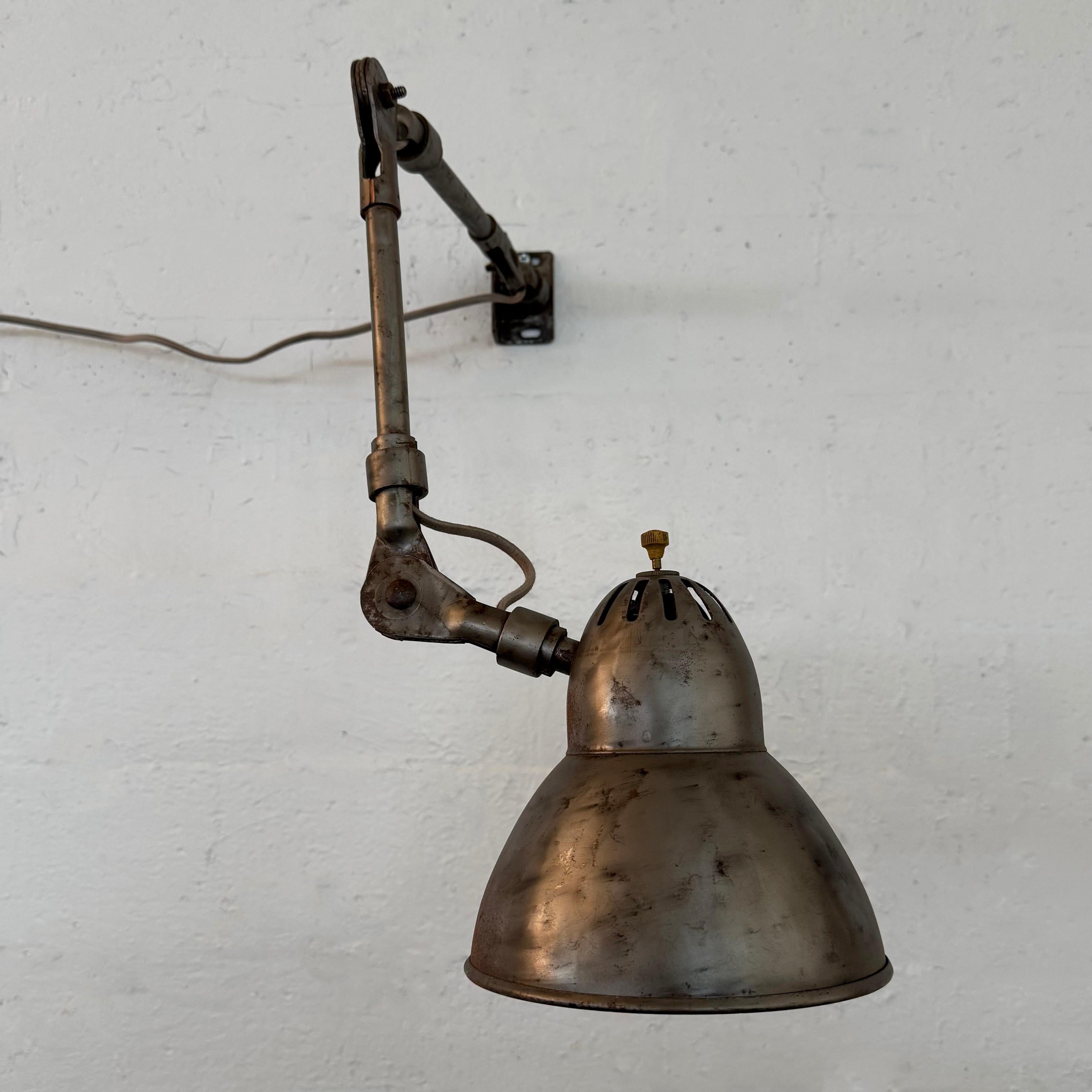 Cette lampe de travail industrielle articulée du milieu du XXe siècle présente une finition extérieure en acier brossé et un intérieur peint en blanc avec une patine d'usure parfaite. L'abat-jour en forme de cloche de 6