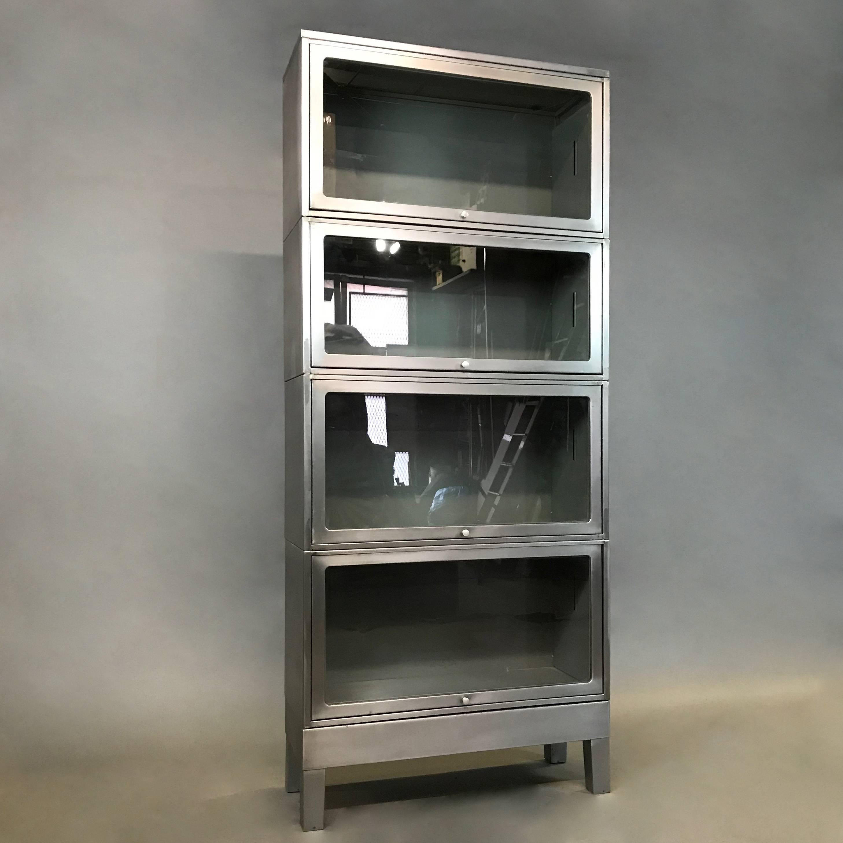 Mid century, Industrial, barrister bookcase, features four interlocking, stackable cases with brushed steel exterior and original gray paint interiors and glass front doors that slide to open. Three cases measure 17