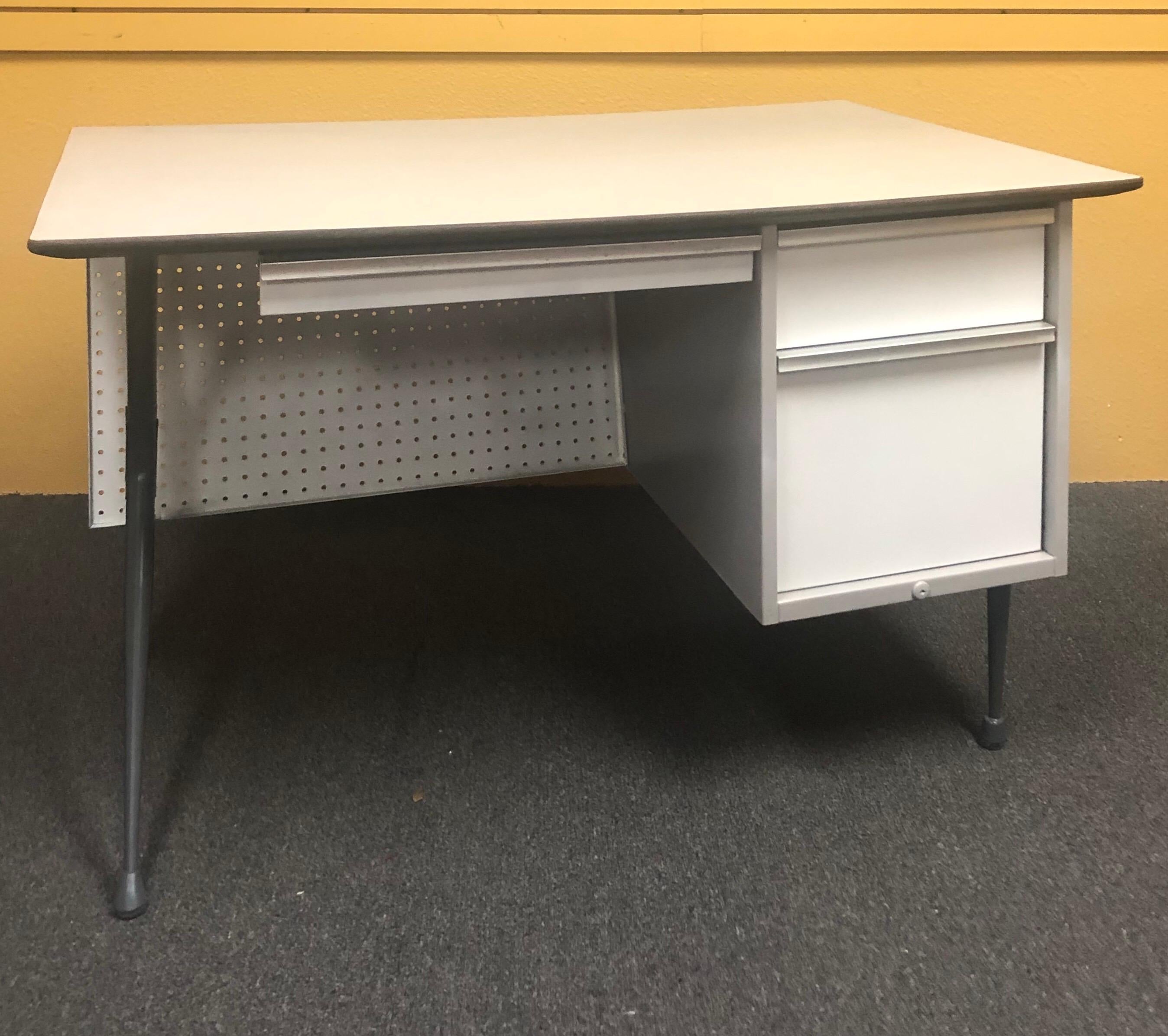 Fantastic industrial midcentury desk by renowned French designer Raymond Loewy for Brunswick of Chicago, circa 1950s. The desk features an exposed metal frame, a unique peg board modesty panel, aluminum trim with original Formica top. It boasts a