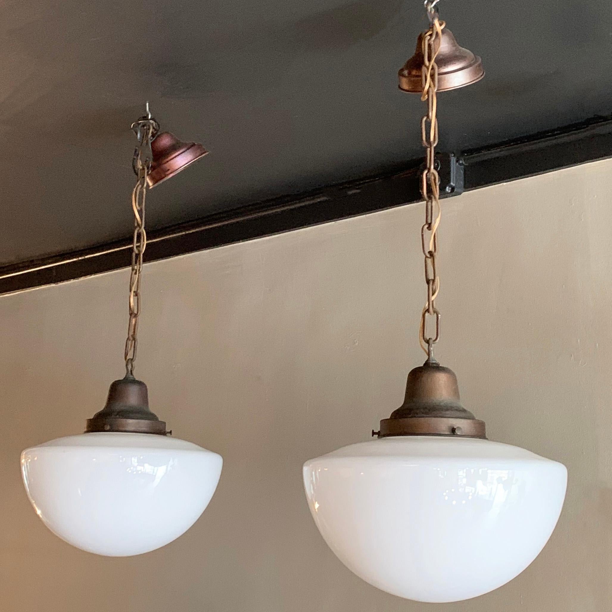 Pair of Industrial, library pendant lights feature button-shaped milk glass shades on brass fitters, chains and canopies that hang down 40 inches using all the chain. The pendants are newly wired to accept up to one 200 watt bulb each.