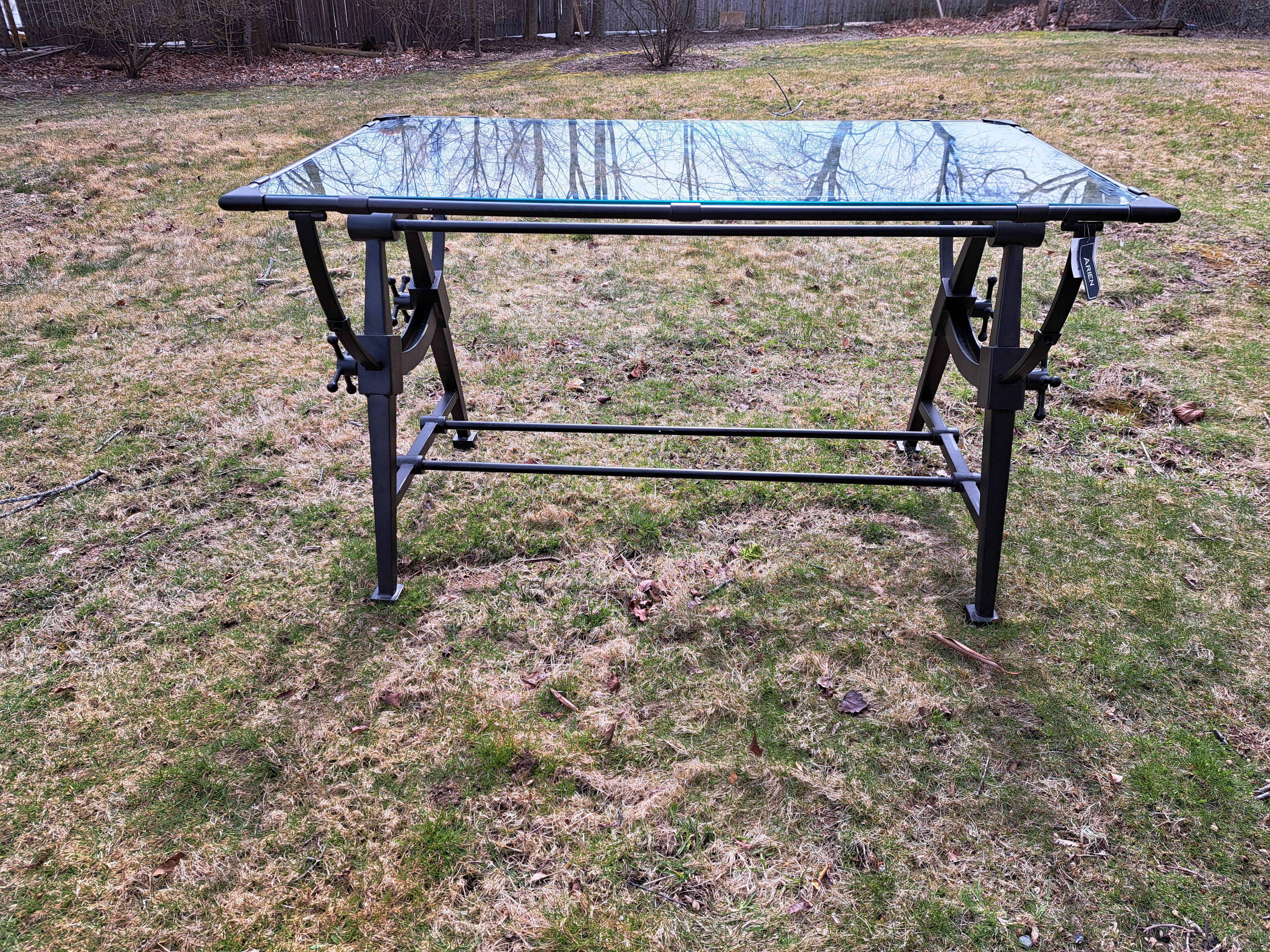 Extraordinary modern wrought iron and glass tilt top drafting desk/table. Glass top is framed by wrought iron and tilts when the steampunk style handles are loosened. Table can be used as a dining or large entrance table.