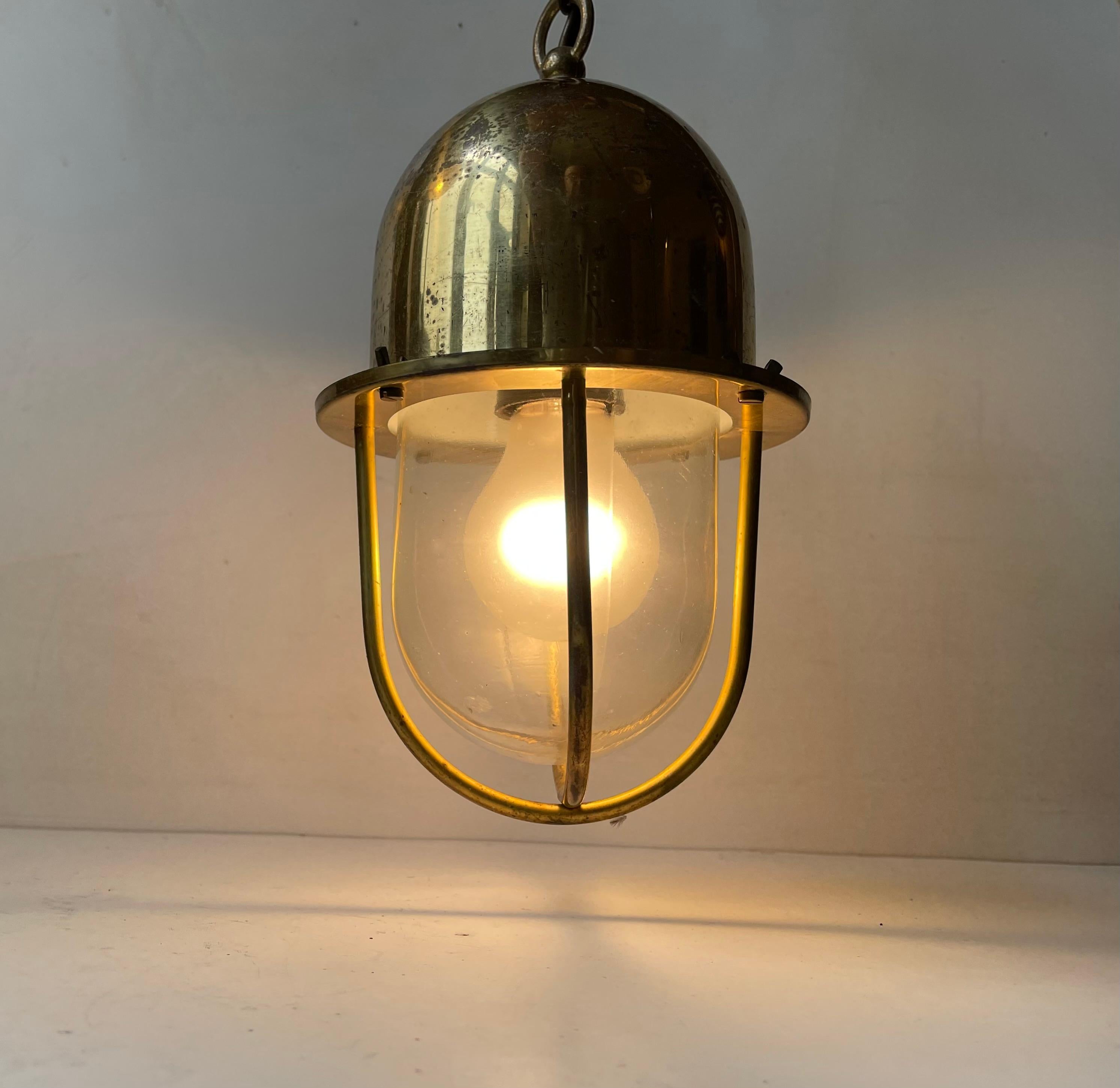 Raw and authentic looking industrial ship lamp in solid brass featuring an inner-dome in clear glass. It was made by ABO Randers in Denmark during the 1970s. It comes chain suspended and with its original brass canopy with matching patina.