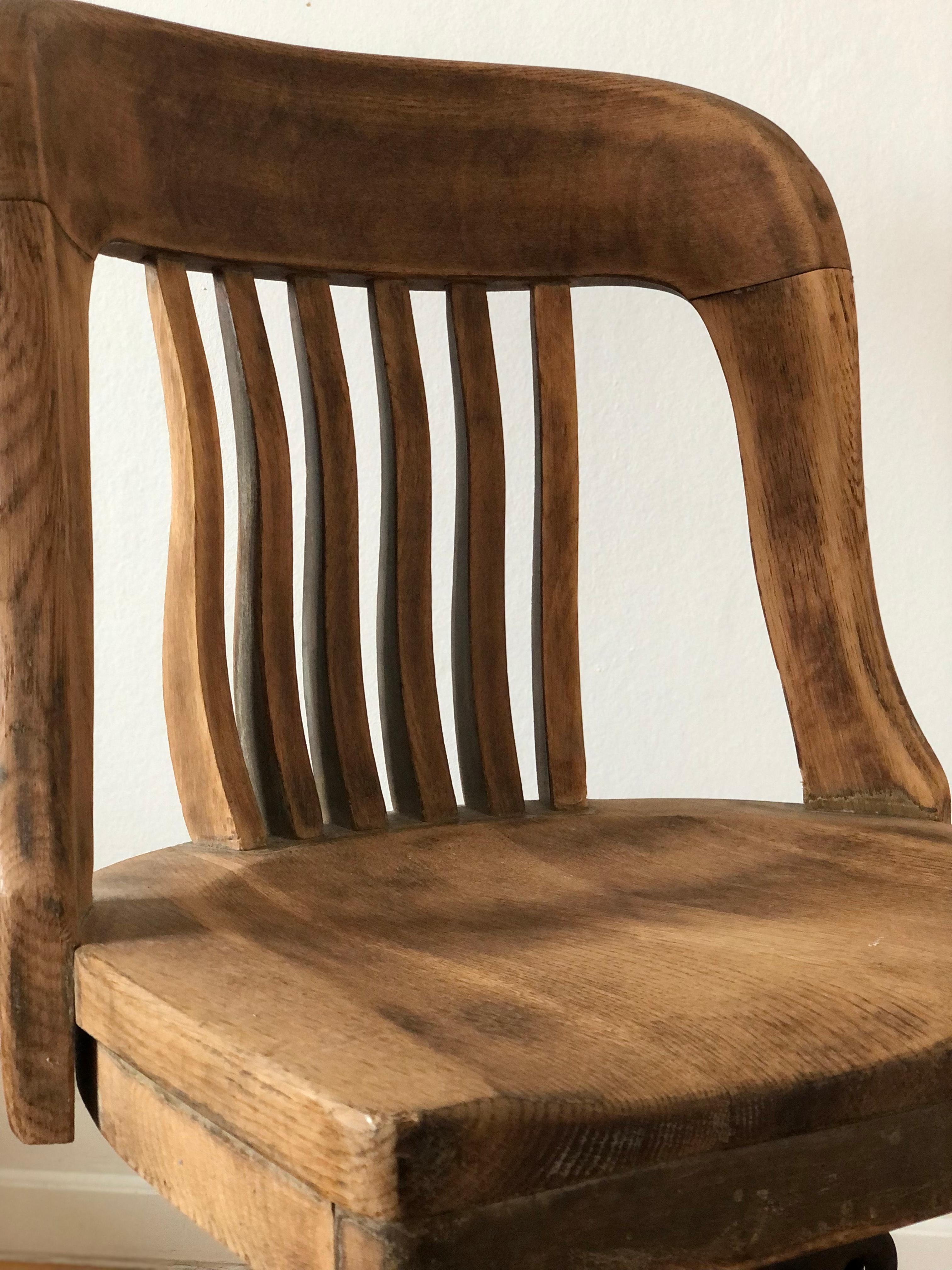 This early 20th-century oak desk chair features a spindle back and a shaped seat for added comfort. The chair is mounted on old casters and equipped with a steel swivel mechanism, allowing for smooth height adjustment. Its industrial design and