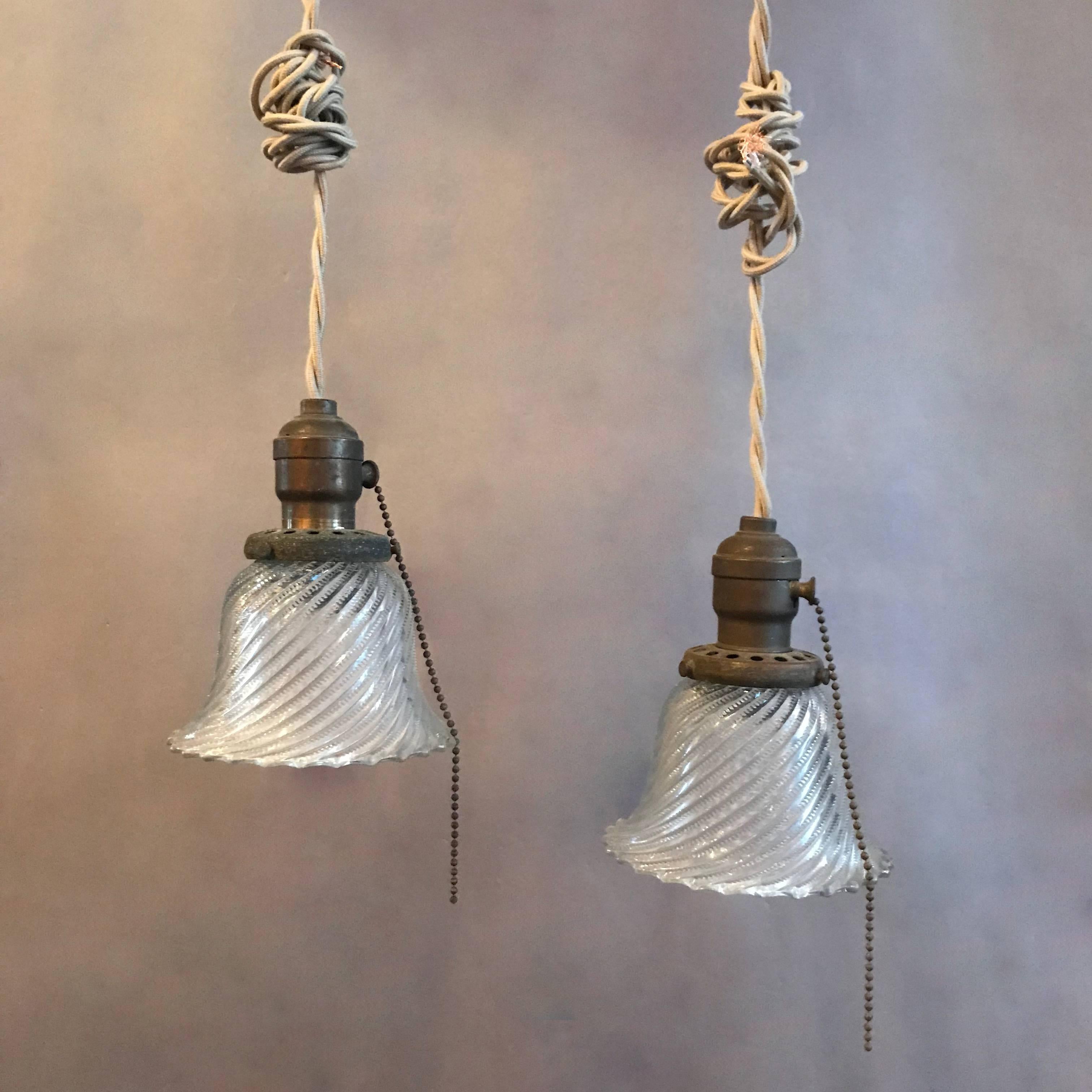 Industrial, diagonal swirled, Holophane pendant lights feature bell shaped shades with ruffled edges and brass fitters with pull chains. These lights are newly wired with 48in. of braided cloth cord.