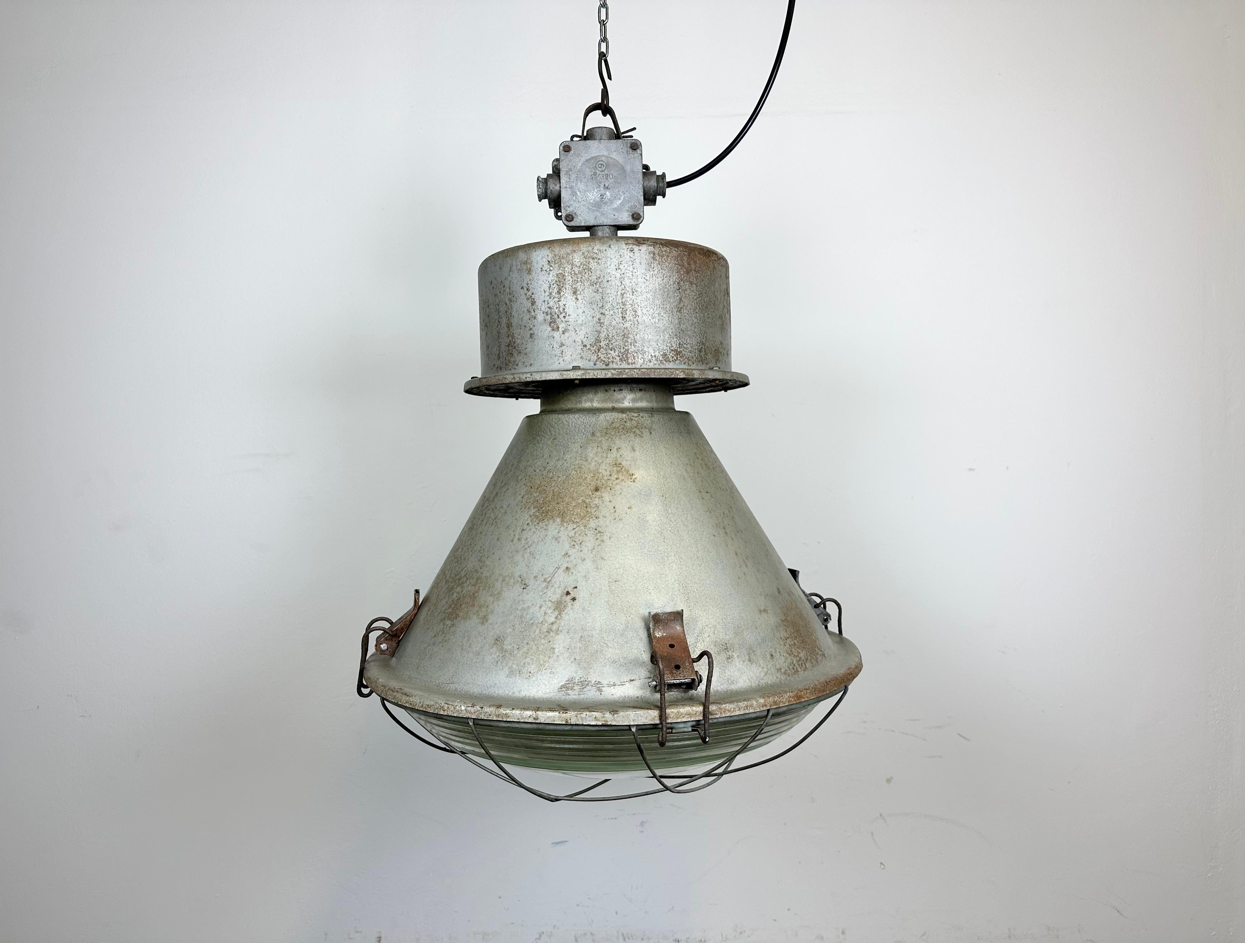 Vintage industrial hanging lamp manufactured in 1970s by MESKO in Skarzysko-Kamienna in Poland. It features a grey iron body, a cast aluminium top, iron grid and clear glass cover. The porcelain socket requires E 27/ E26 light bulbs. New wire. The