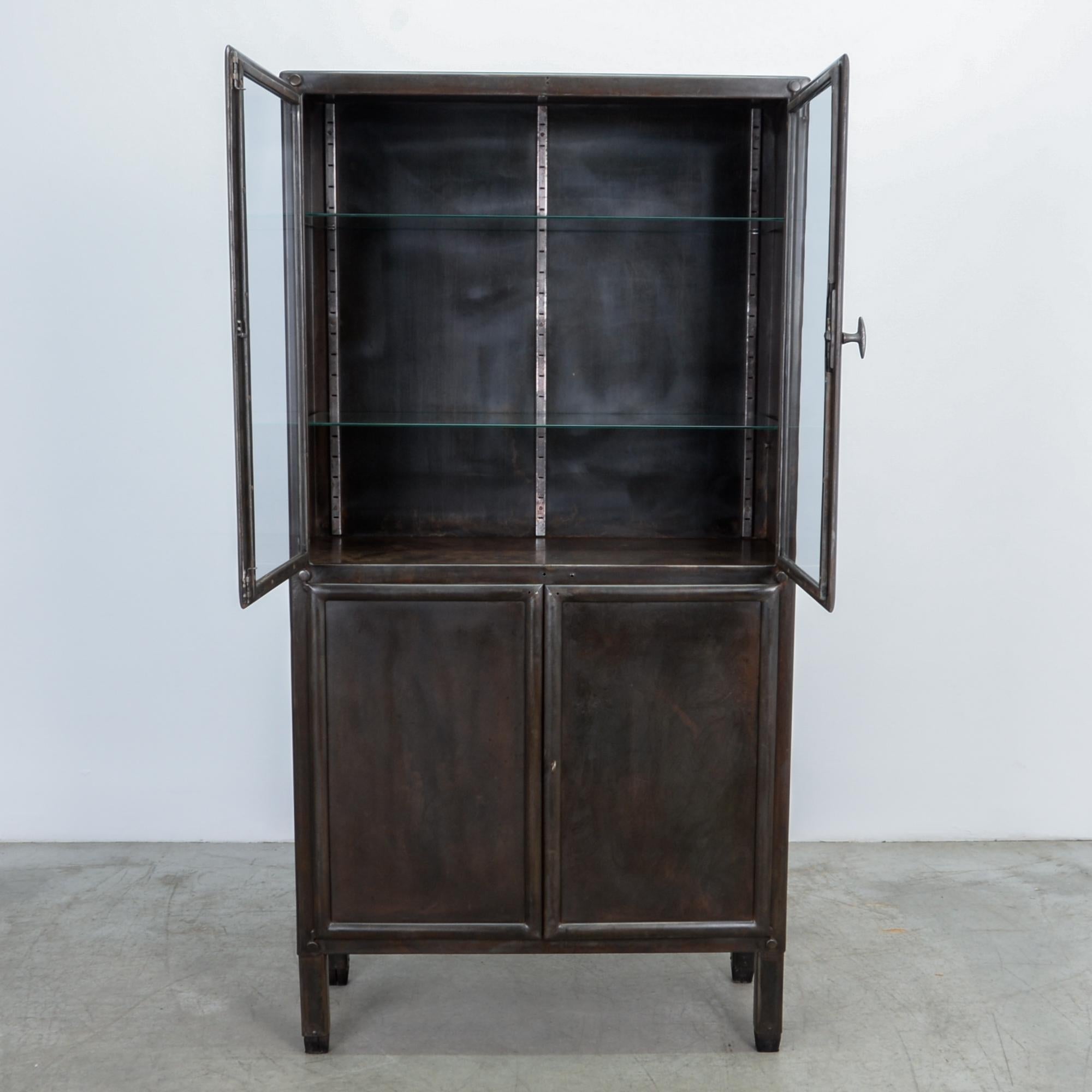 A four-door tall metal vitrine from Czech Republic, circa 1950. This polished steel cabinet was originally designed for Industrial use. The glass interior shelves, and textured steel backdrop make a great frame for display.