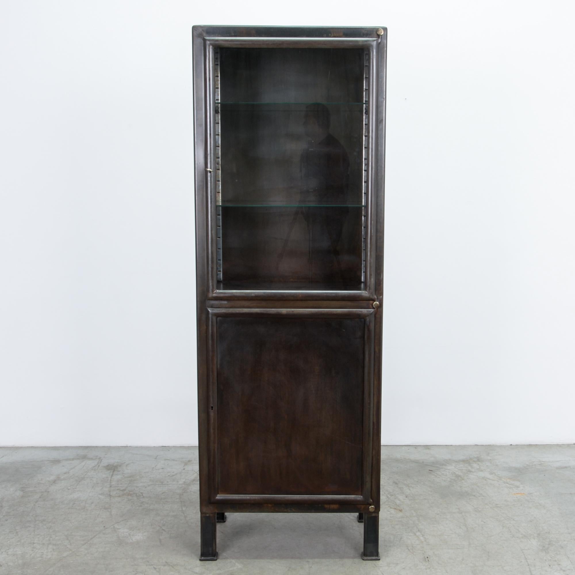 A two door tall metal vitrine from Czech Republic circa 1950 with characteristic industrial oxidised patina. This polished steel cabinet was originally designed for industrial use. The glass interior shelves, and textured steel backdrop make a great