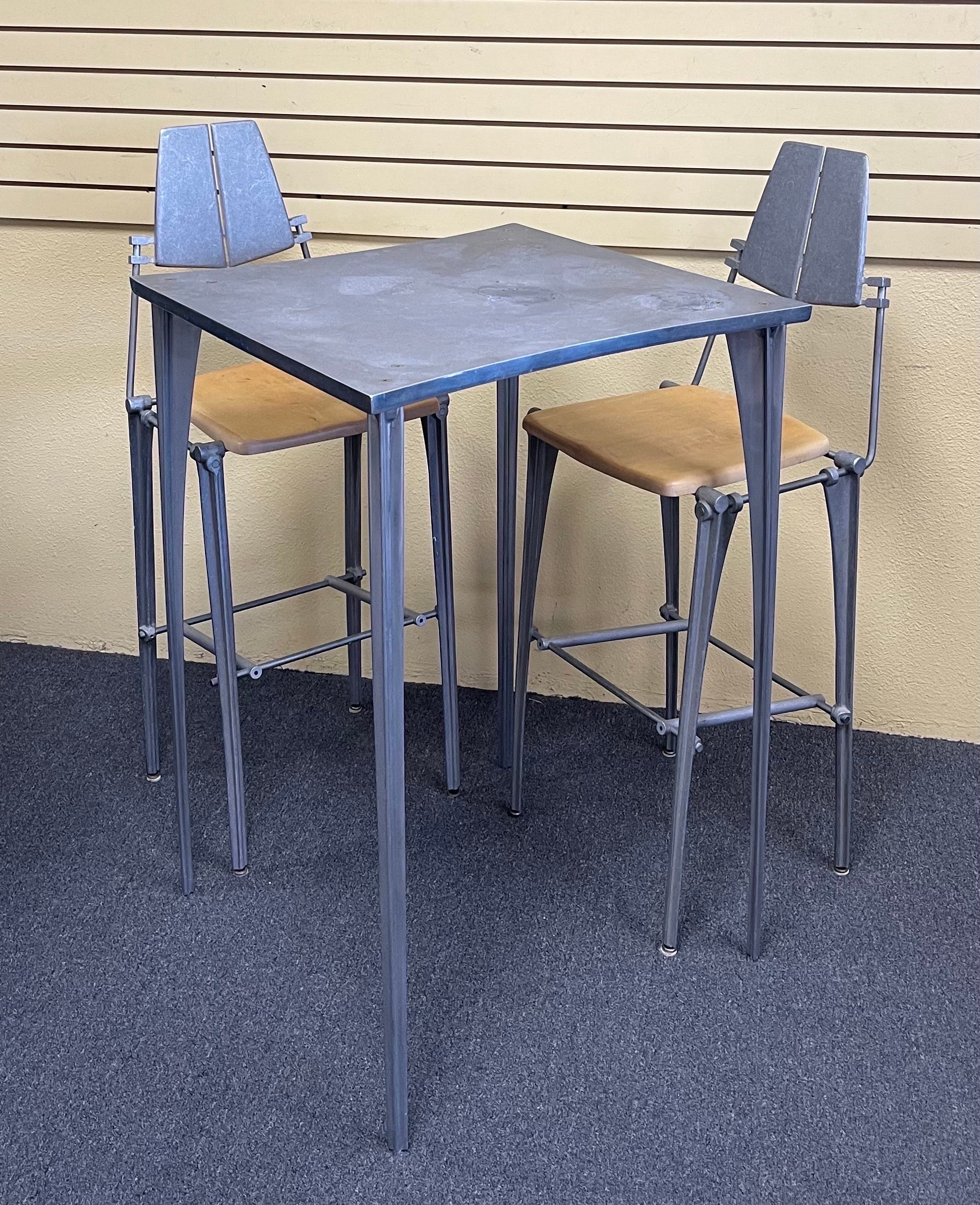 Industrial post-modern design bar height table and two stools by Robert Josten, circa 1970s.  The table and the stool frames are made of cast aluminum with solid maple seats.  The bistro table measures 28