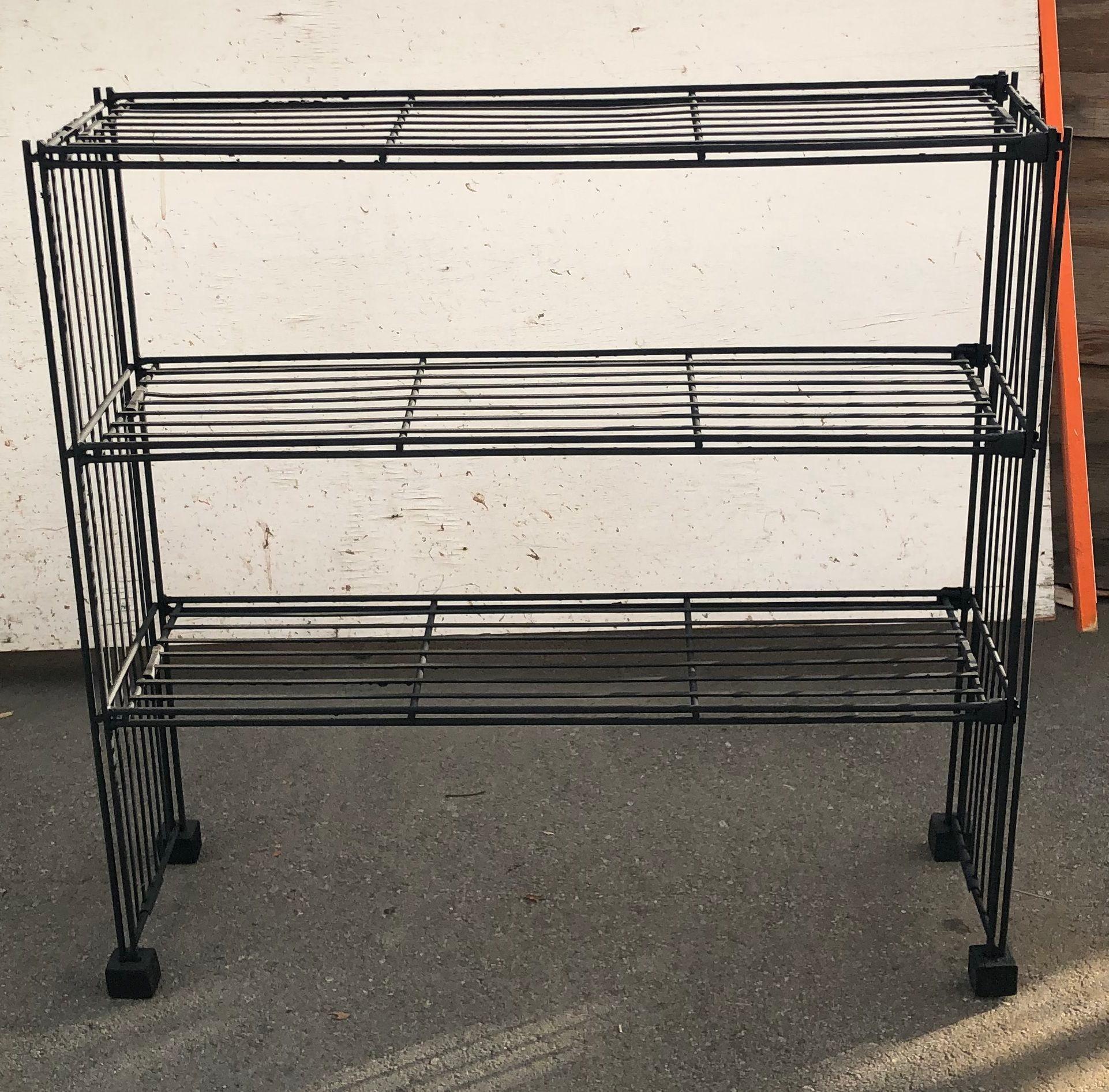 Mid-Century black iron storage rack with black block feet.

Crafted from sleek black iron, this storage rack channels the industrial era's robustness while embracing postmodern design's bold and unconventional characteristics. Its geometric lines,