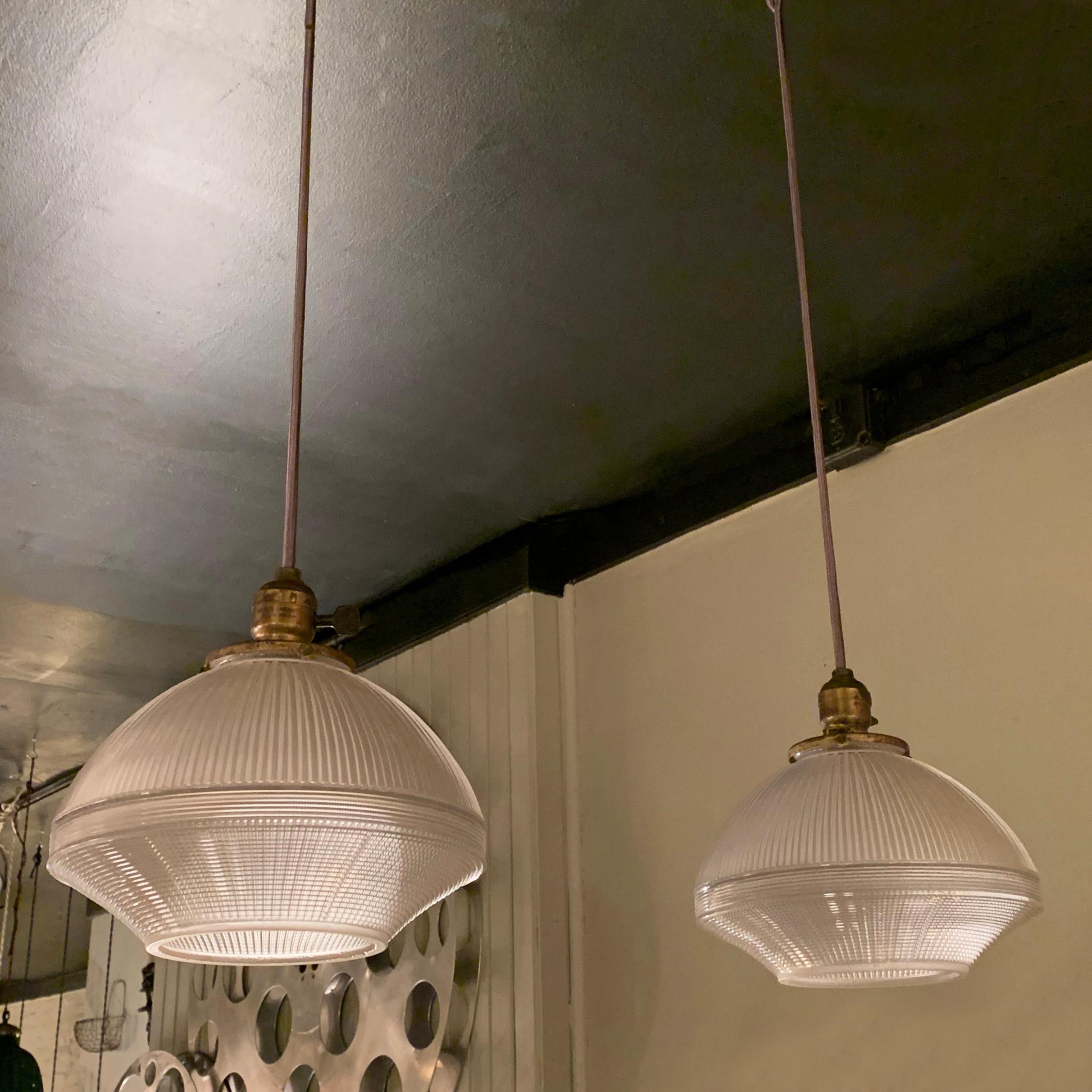 Pair of industrial, factory pendant lights feature prismatic, Holophane glass shades with open bottoms on brass paddle switch fitters, newly wired with 40 inches of gray cloth cord to accept up to a 200 watt bulb each.