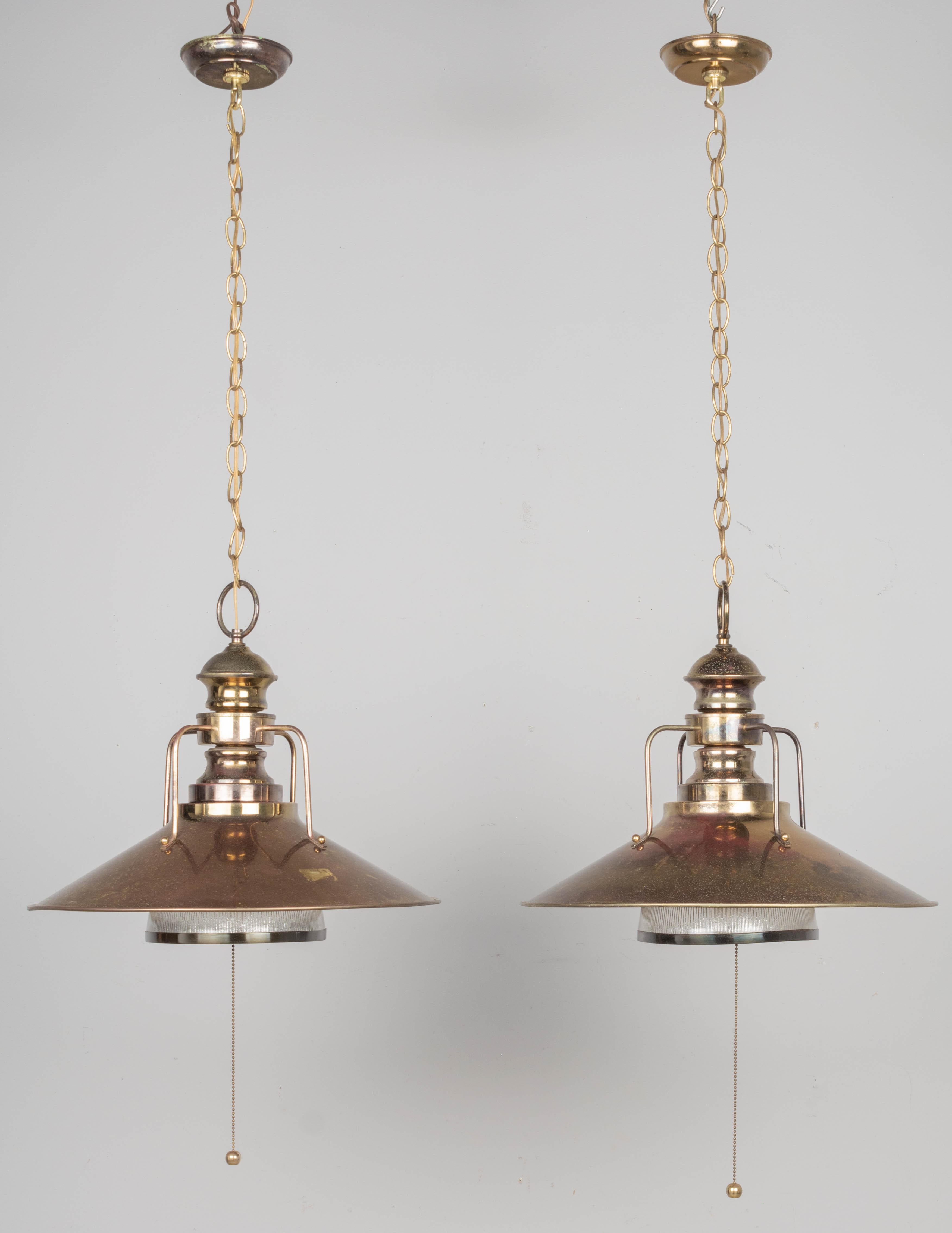 A pair of industrial railway station brass plated pendant lights with holophane glass reflector shades. Beautiful worn aged patina with warm color variegation and pitting. These lamps are in working condition and appear to have been rewired at some