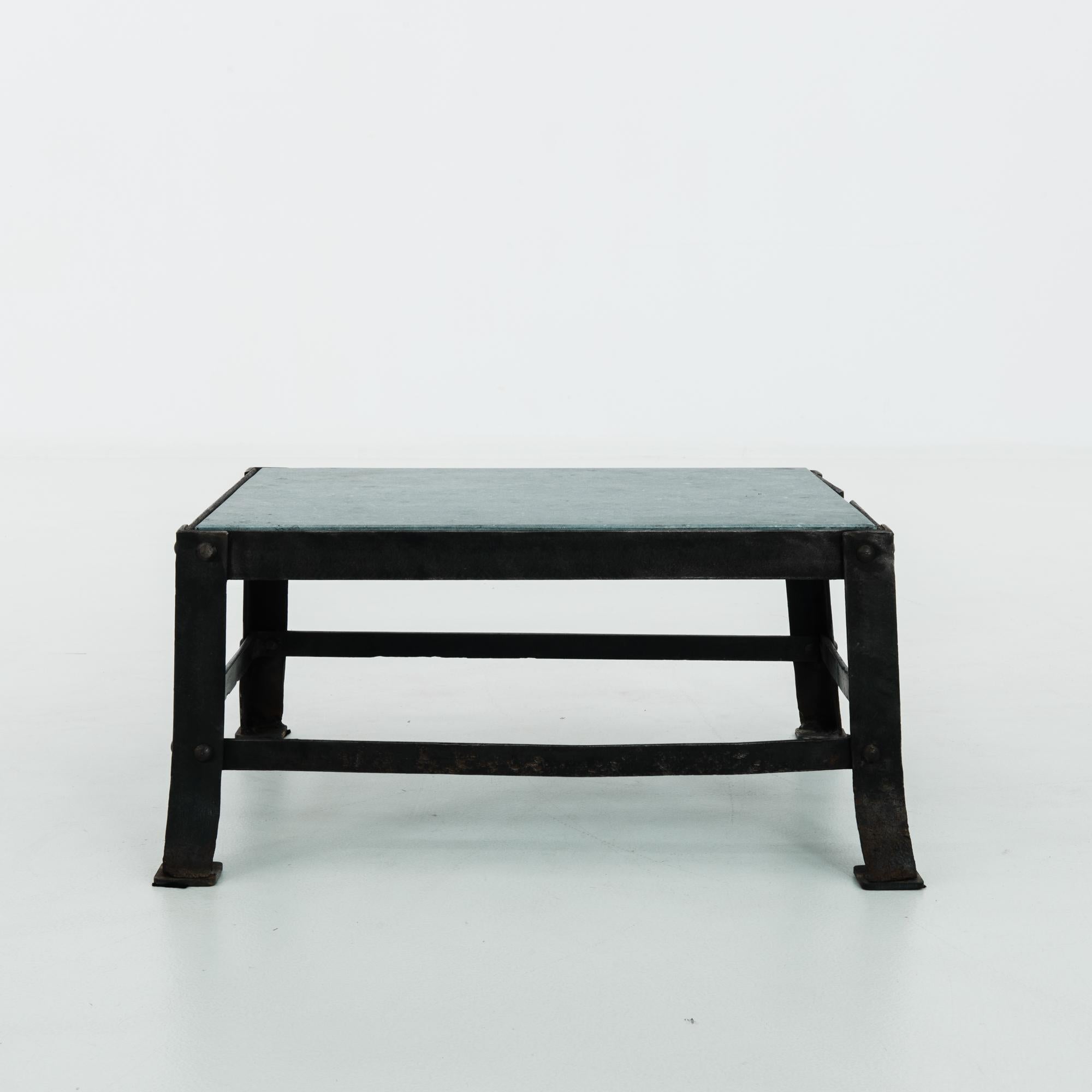 A stone topped metal table from Belgium, circa 1900. The steel frame creates a structural base, thick metal bars are riveted firmly in place, echoing the industrial effect. Metallic iron is softened by a black polished finish, while a slab of