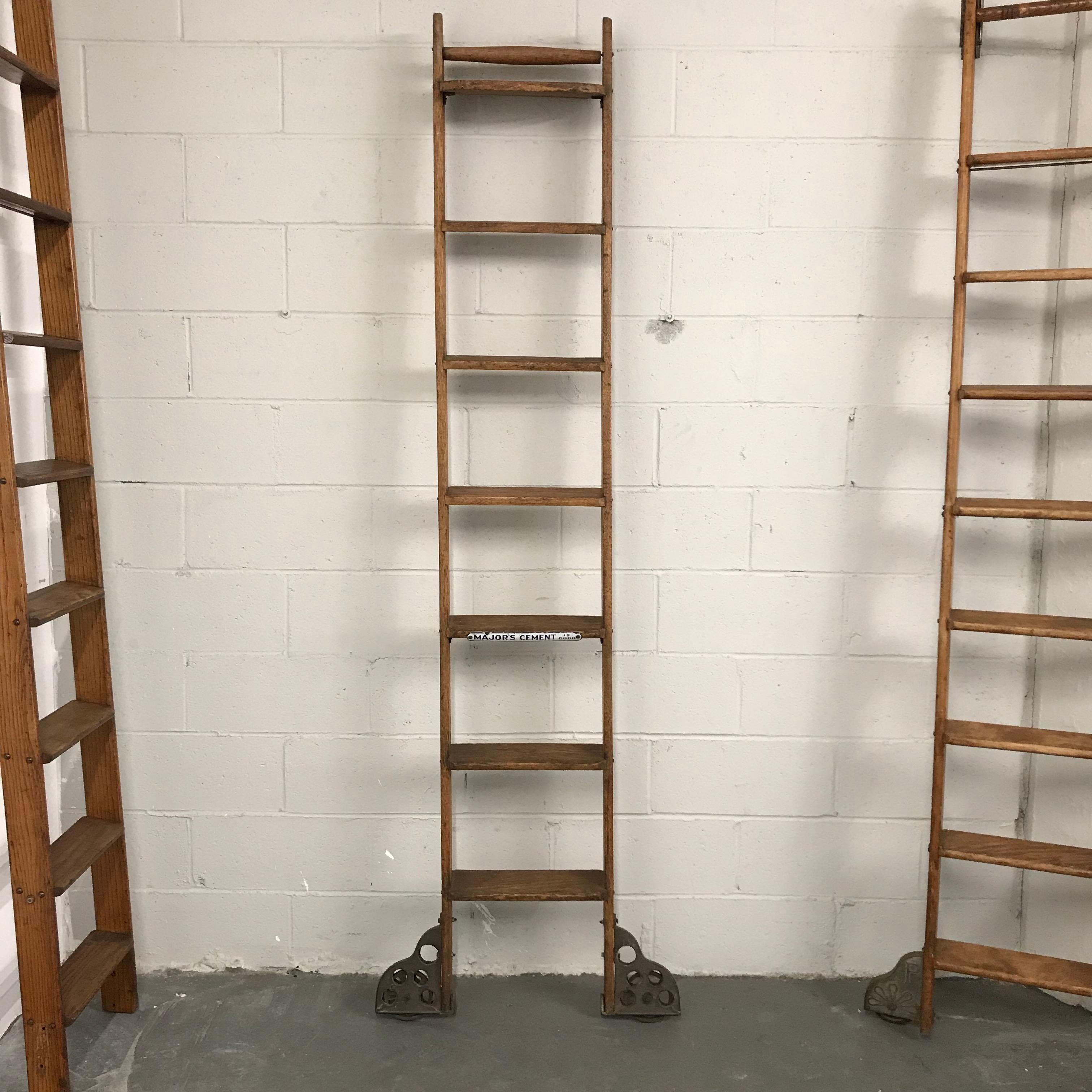 Industrial, rolling, oak ladder by Putnam features decorative steel lateral wheels at the bottom with a porcelain enameled advertising plaque for Major's Cement. The rungs are 4 inches wide and the wheels measure 28 inches wide.