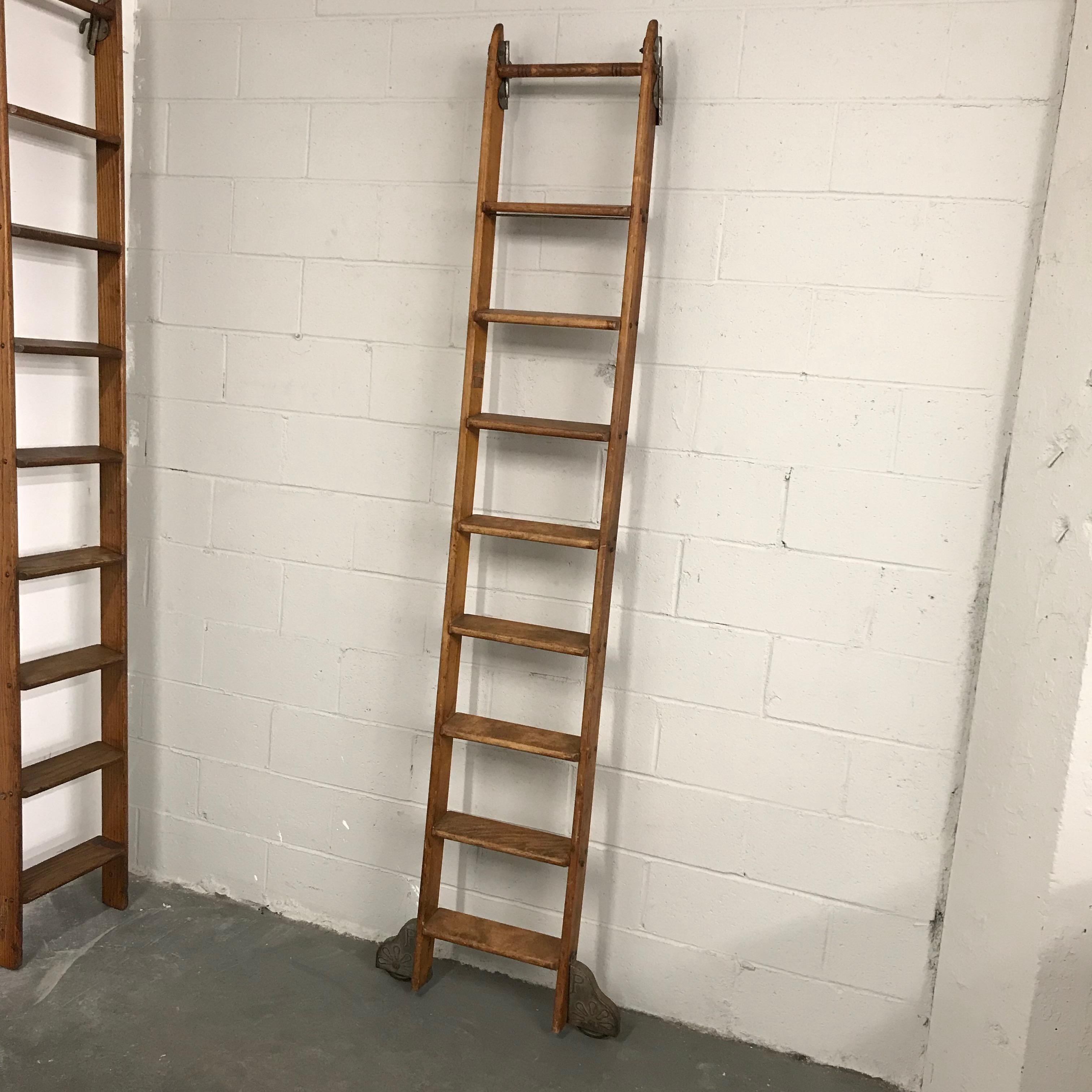 Industrial, rolling, oak library ladder by Putnam features decorative steel hardware, hooks at the top and lateral wheels at the bottom. The rungs are 4 inches wide and the wheels measure 27 inches wide.