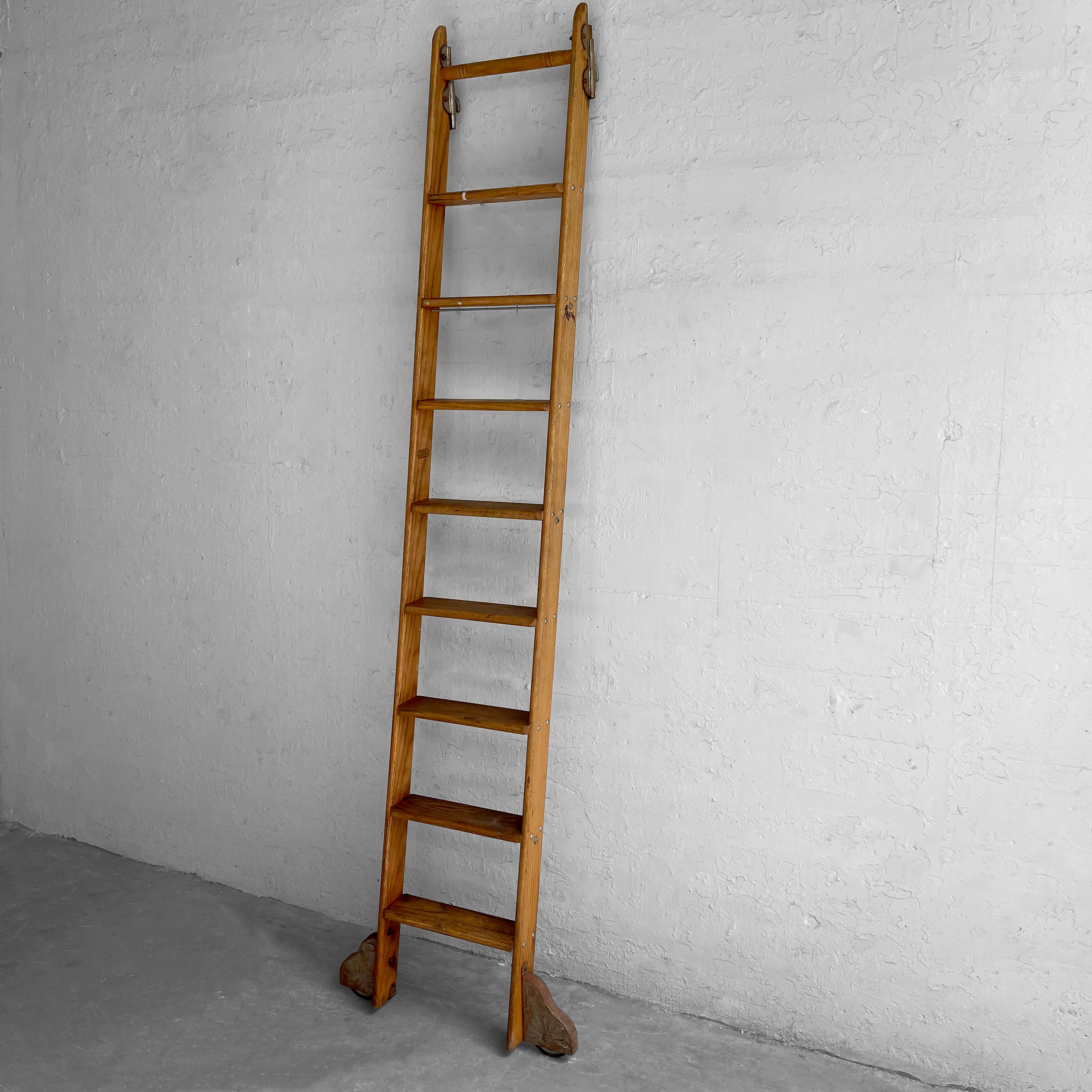 Industrial, work-worn, rolling, oak library ladder by Putnam features decorative steel hardware, hooks at the top and lateral wheels at the bottom that measure 27 inches wide. The ladder width is 16 inches.