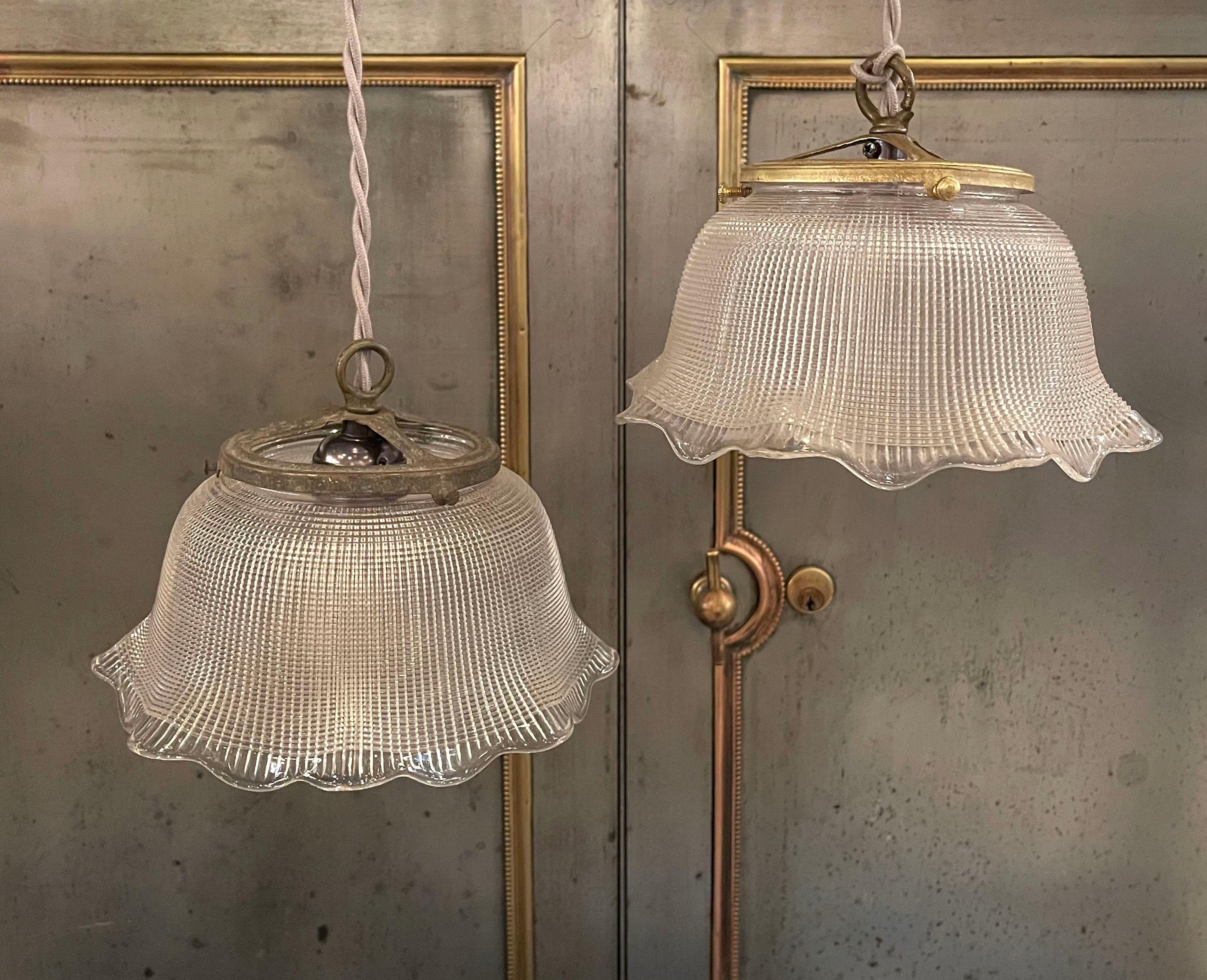 Industrial, ruffled bell-shaped, prismatic, Holophane glass pendant lights with brass fitters and sockets are newly wired with braided gray cloth cord. The pendants hang at an overall height of 80.5 inches. 2 pendants are available, sold