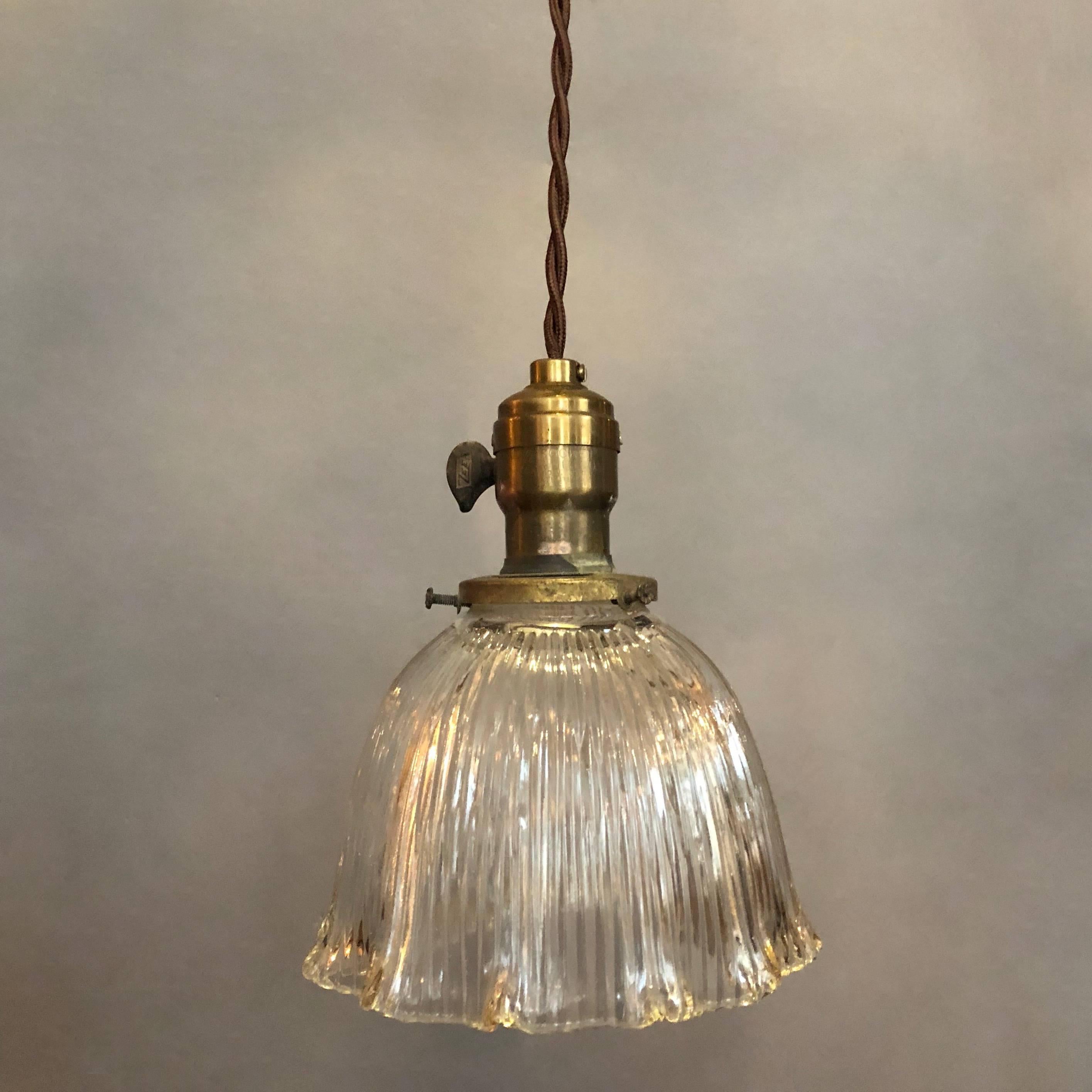 Lampe pendante industrielle du début du 20e siècle en verre holophane, avec un abat-jour en forme de dôme ou de cloche, profondément découpé, prismatique, avec un bord festonné, une armature en laiton avec un interrupteur à palette et un cordon de